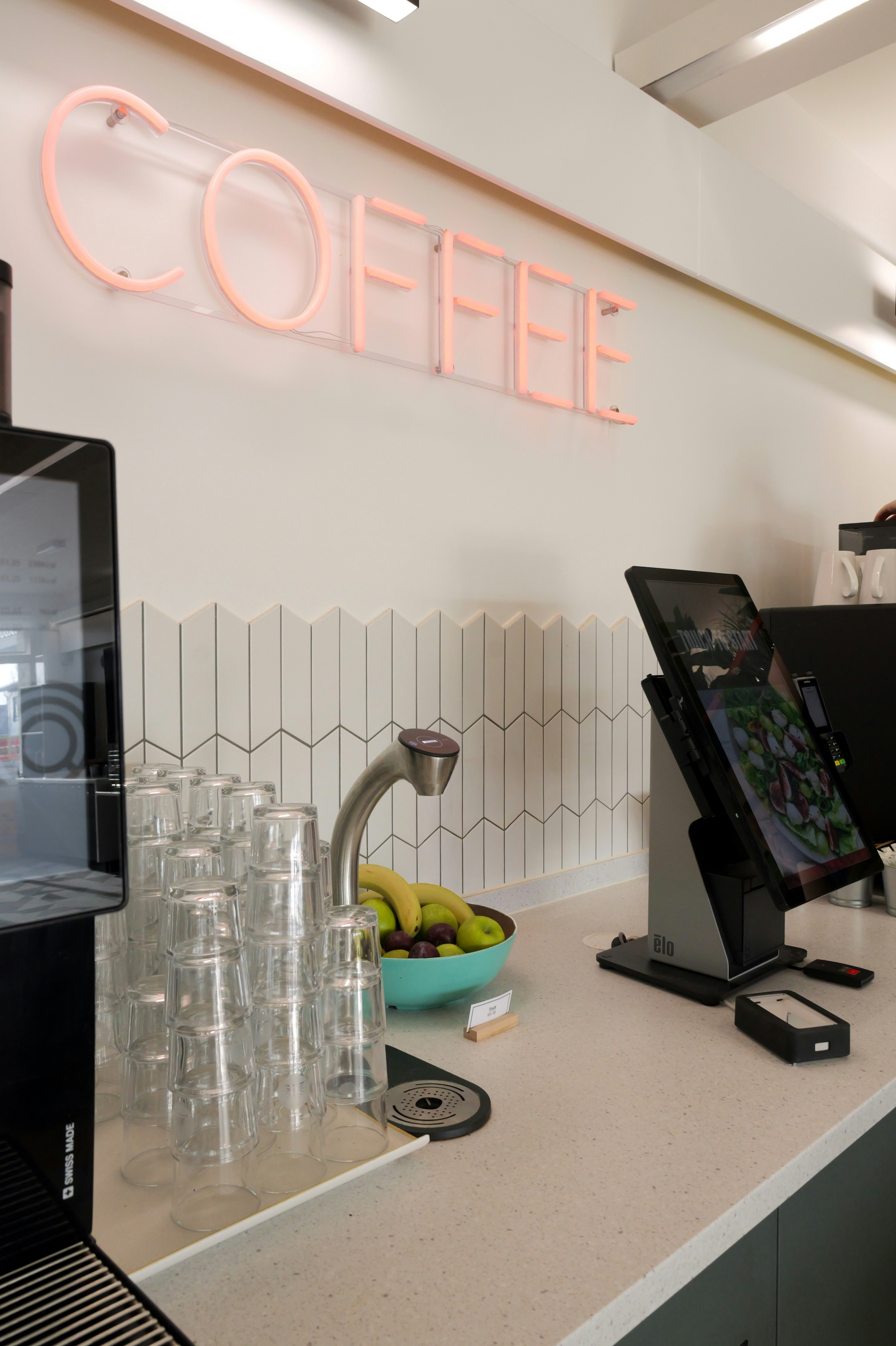 A neon sign reading COFFEE above a counter with glasses and fruit