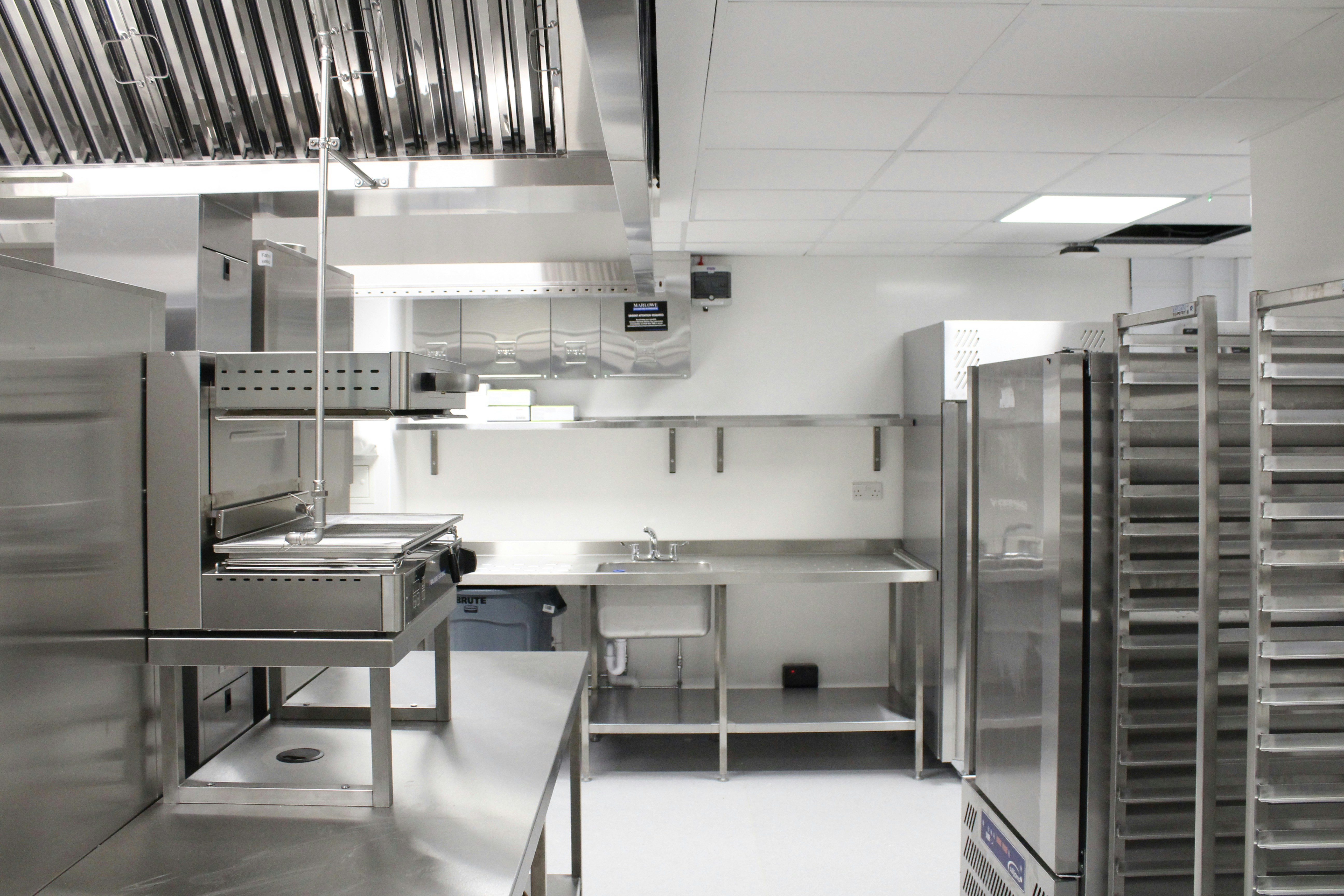 A spotless commercial kitchen with stainless steel benches, ovens and tray racks