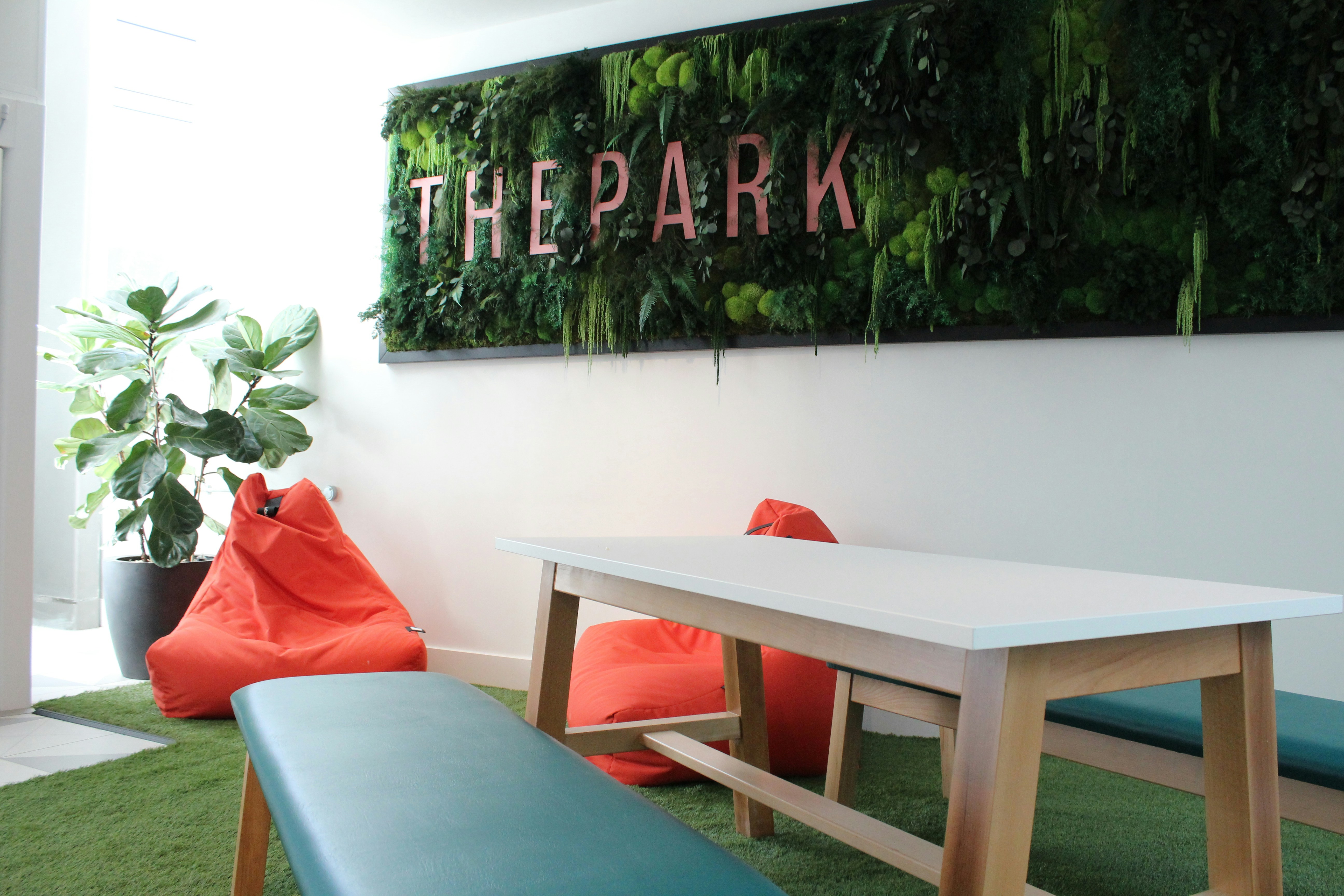 A modern office lounge with orange beanbag chairs, a wooden table, and a green wall