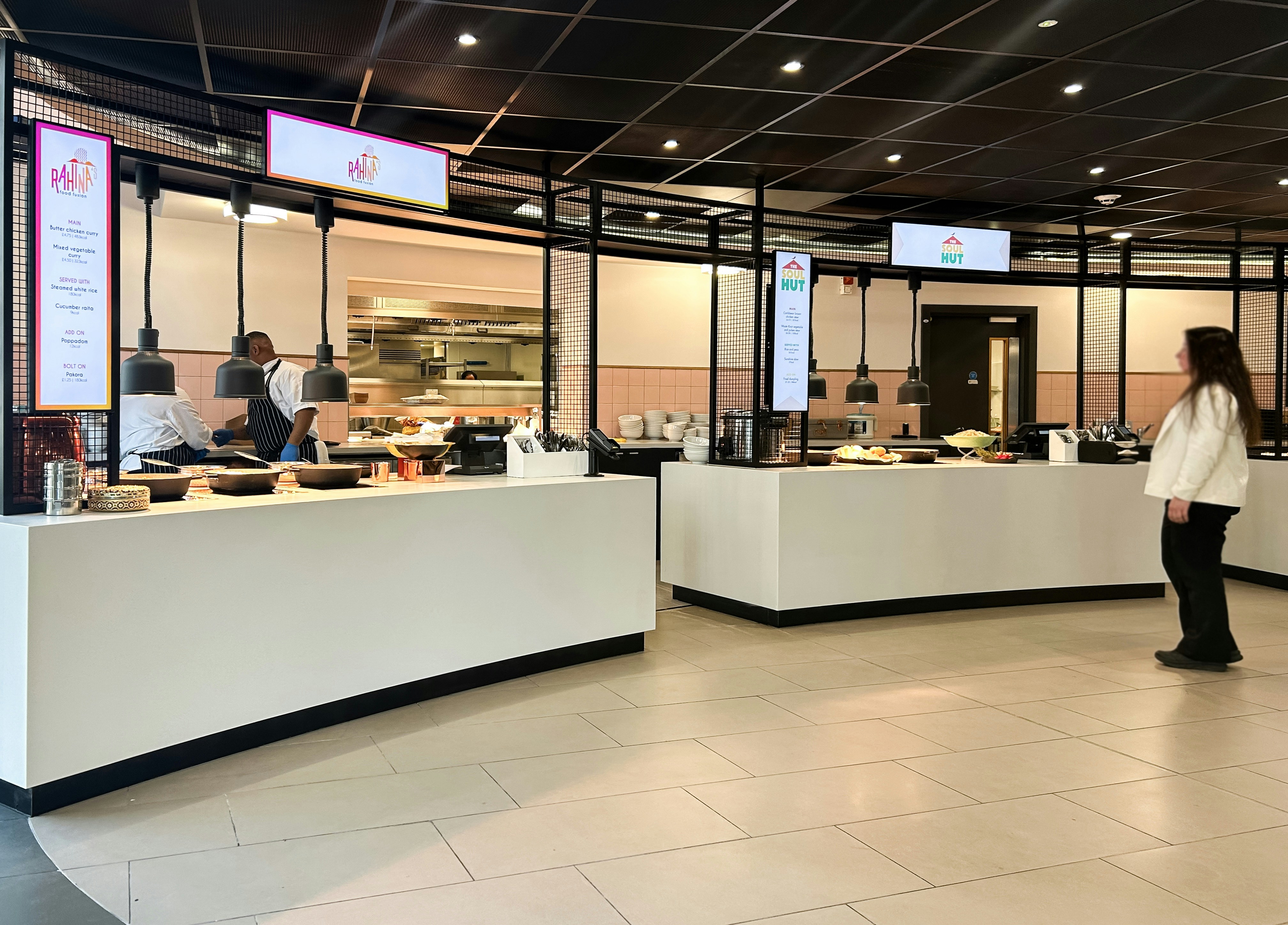 A person standing in a food court with two service counters and chefs
