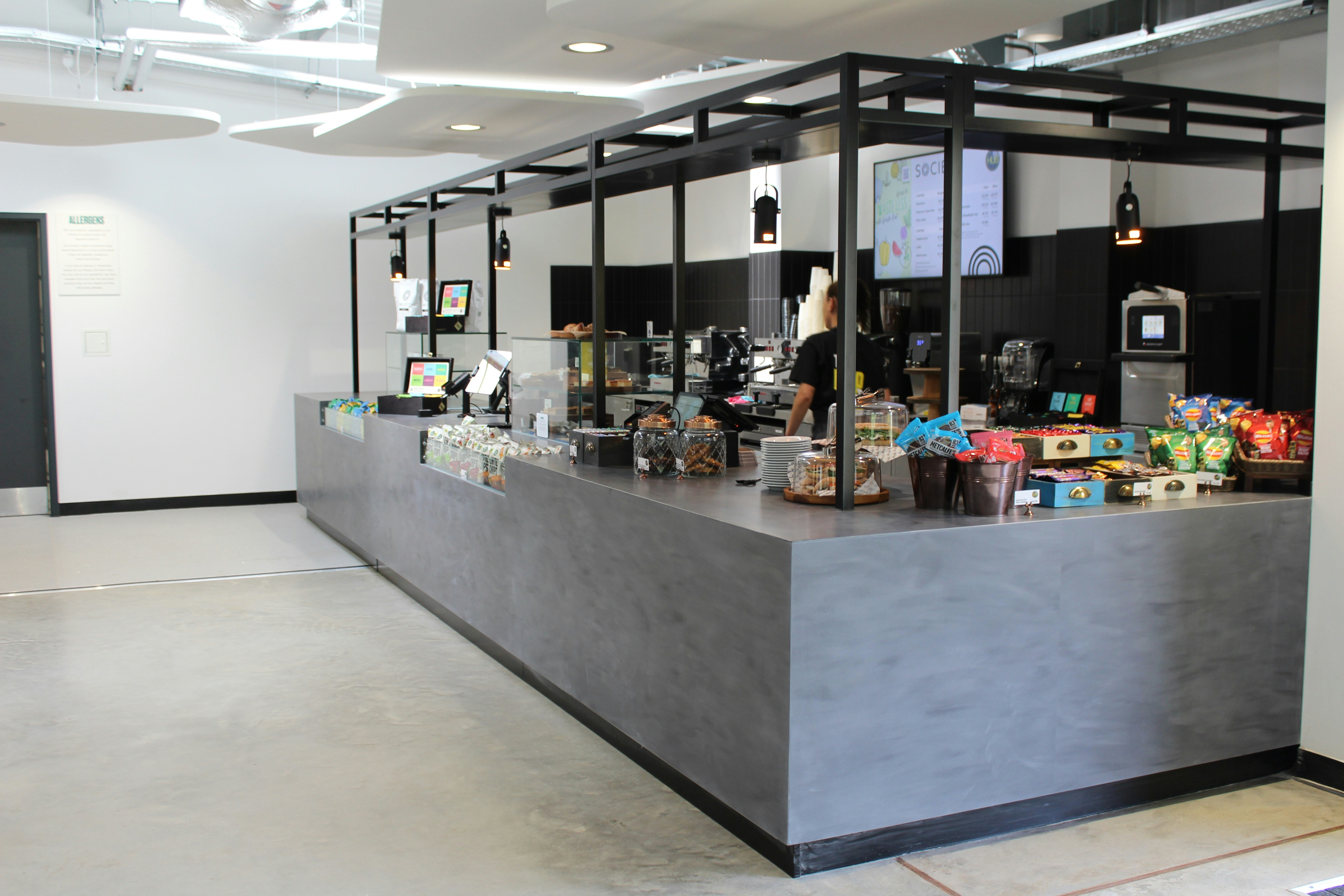 A modern coffee shop counter with grey concrete surfaces and black metal framing