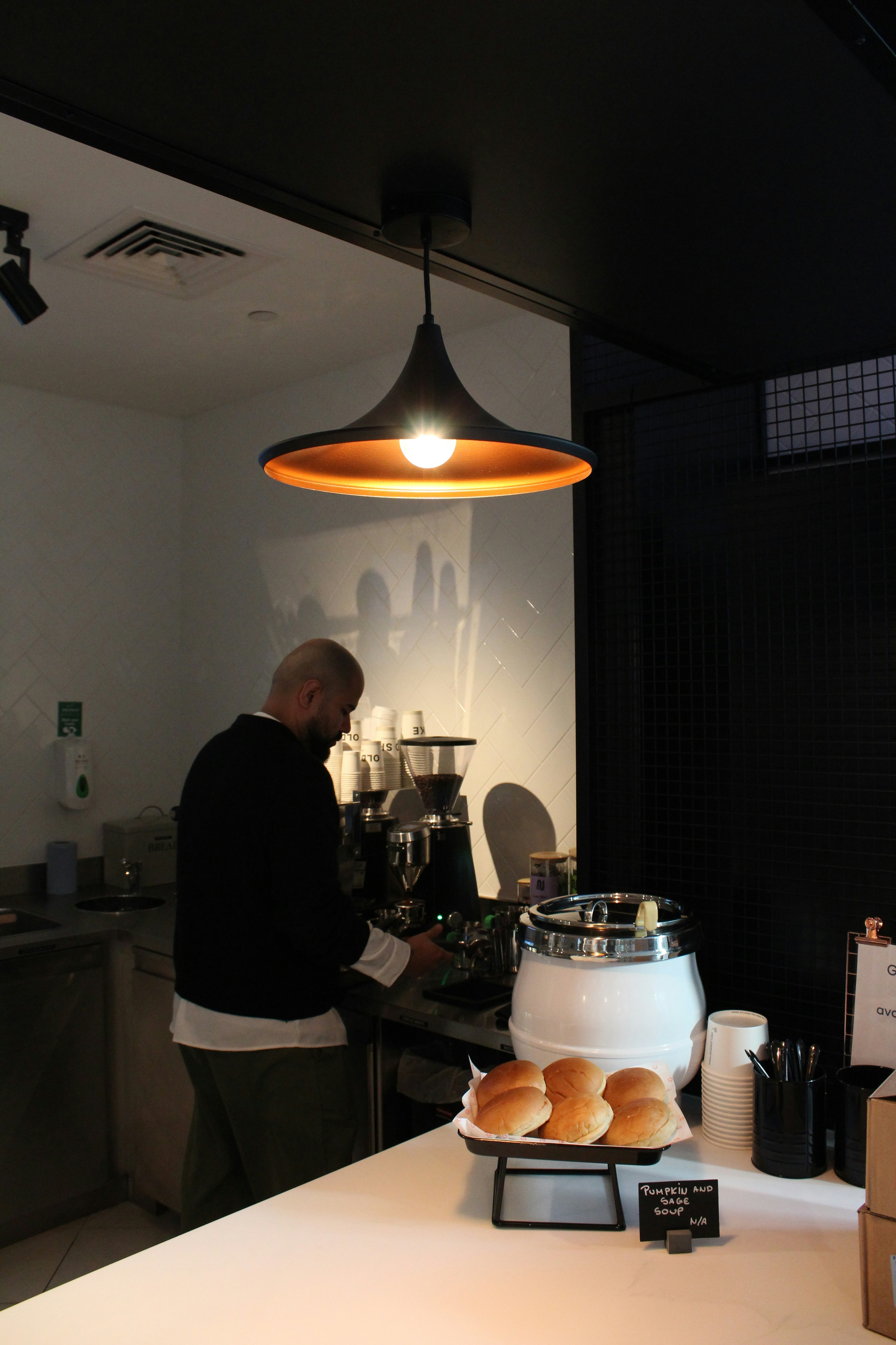 A person preparing coffee behind a counter with buns and soup in a cafe