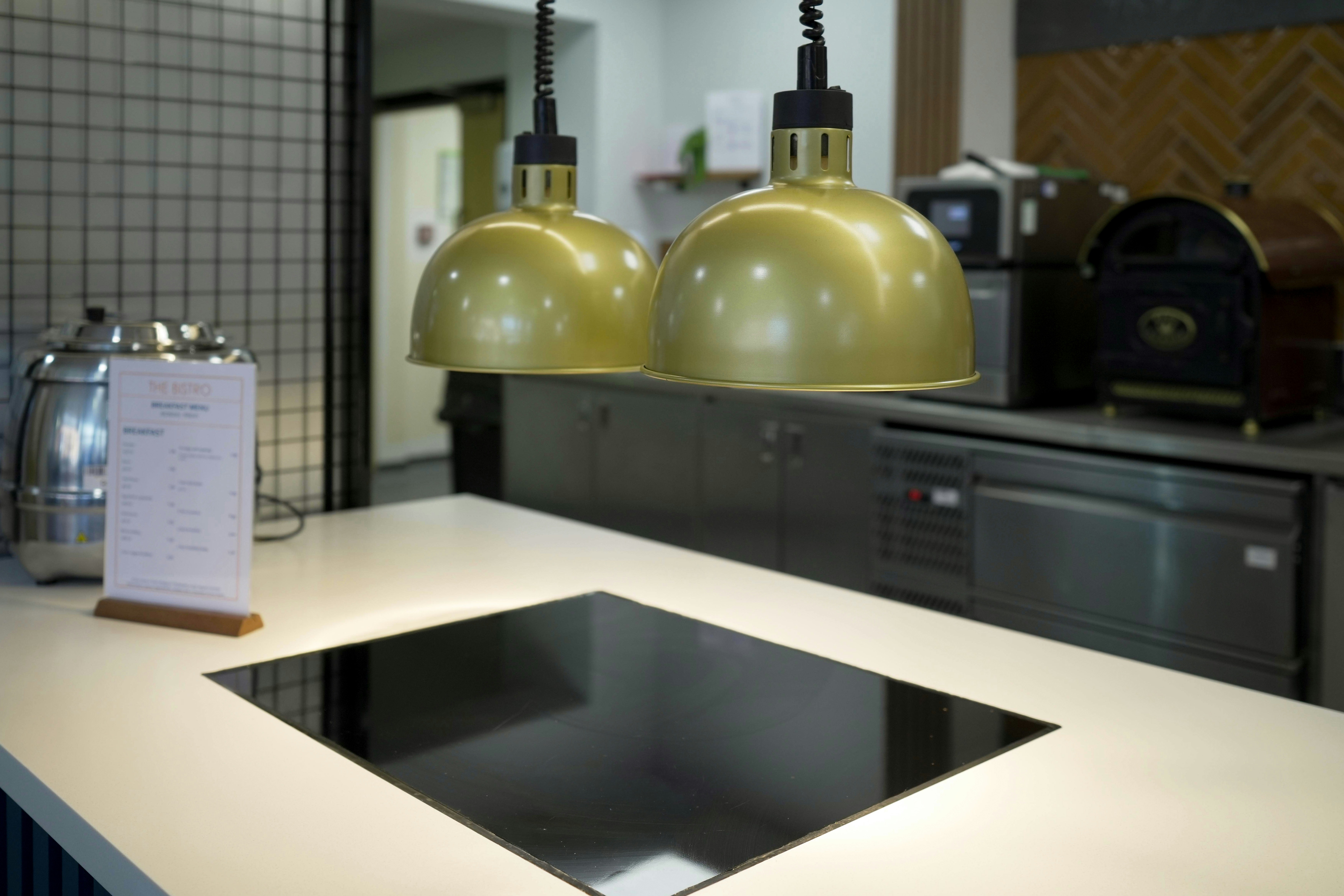 Two gold pendant lights hanging above a black induction cooktop in a kitchen