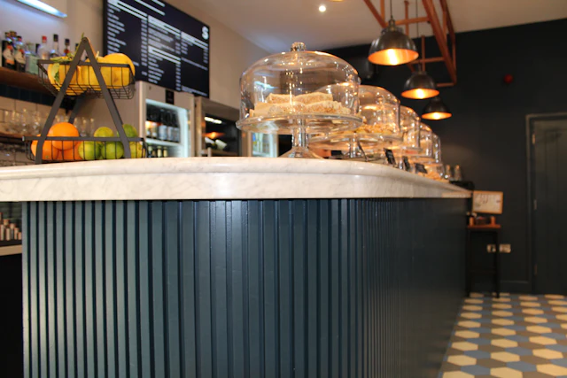 A marble counter with glass cake domes in a dark blue cafe interior