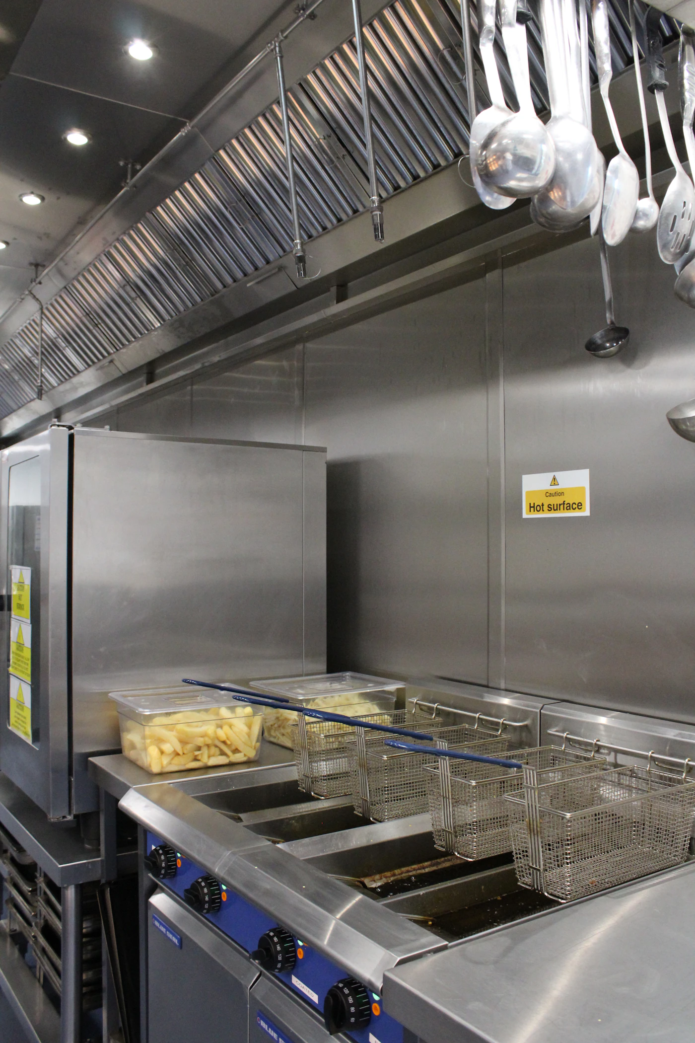 Commercial deep fryers beneath an exhaust hood in a restaurant kitchen