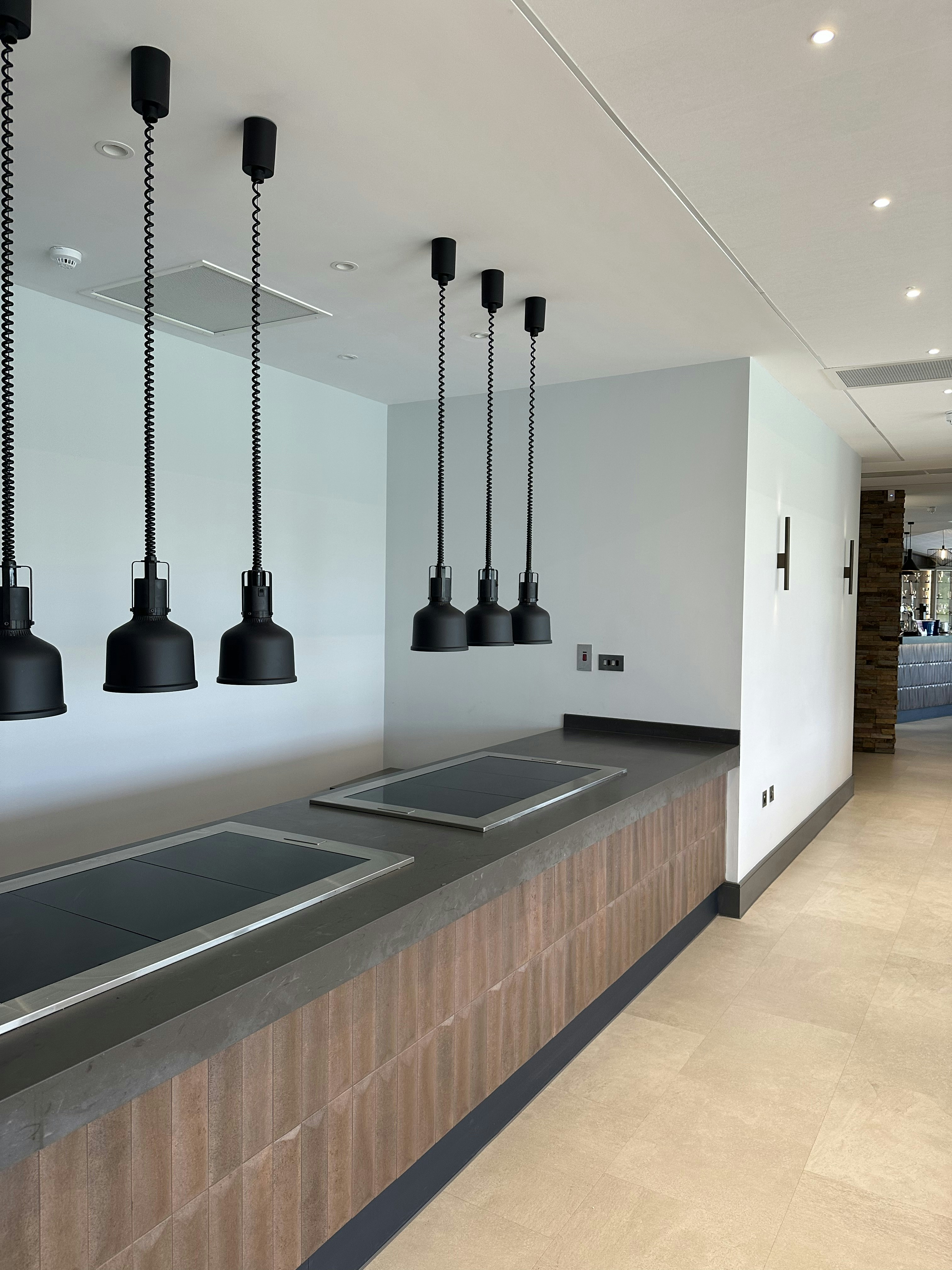Black pendant lights hanging over a long kitchen counter with integrated induction cooktops