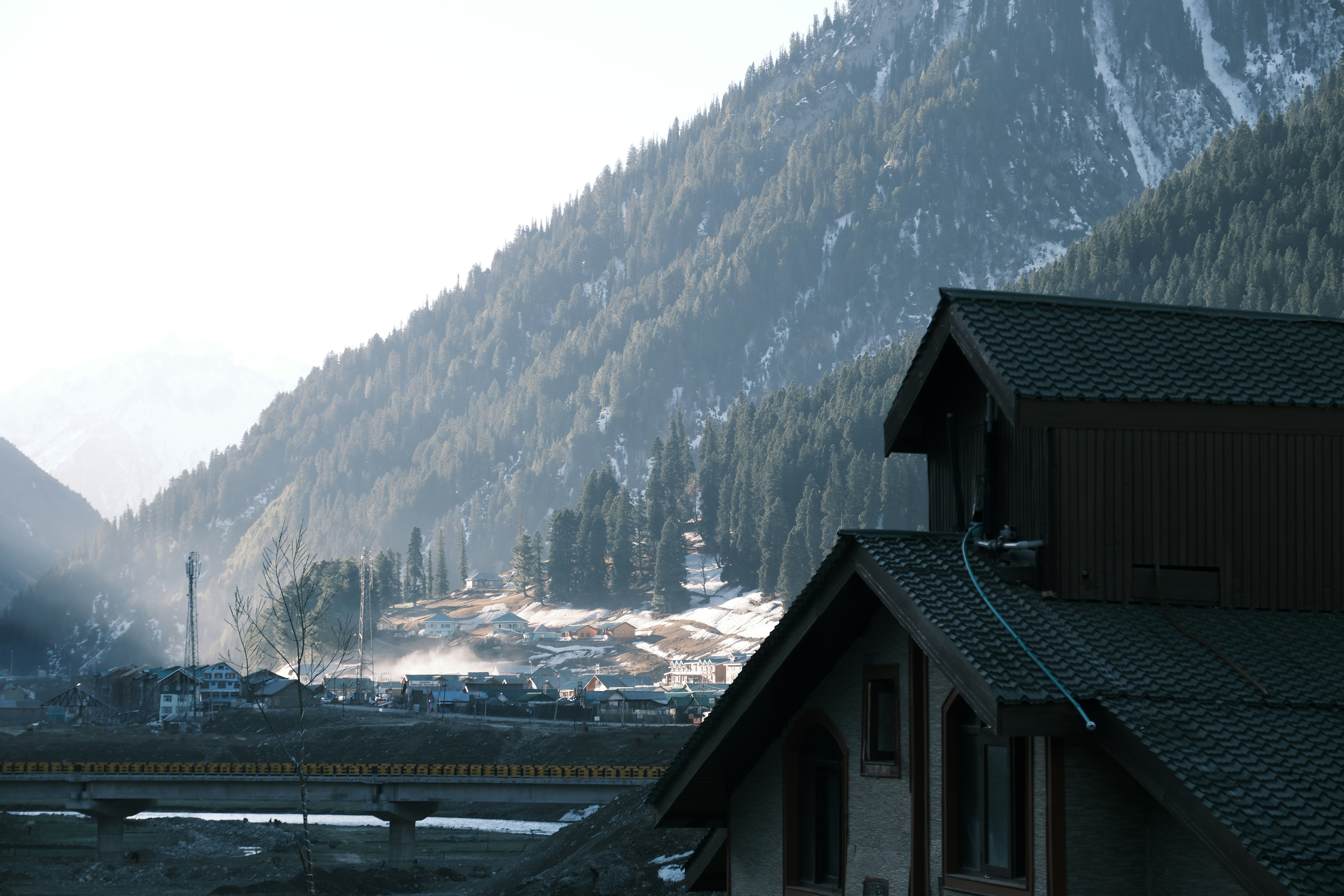A dark house with a gabled roof before a forested mountain slope