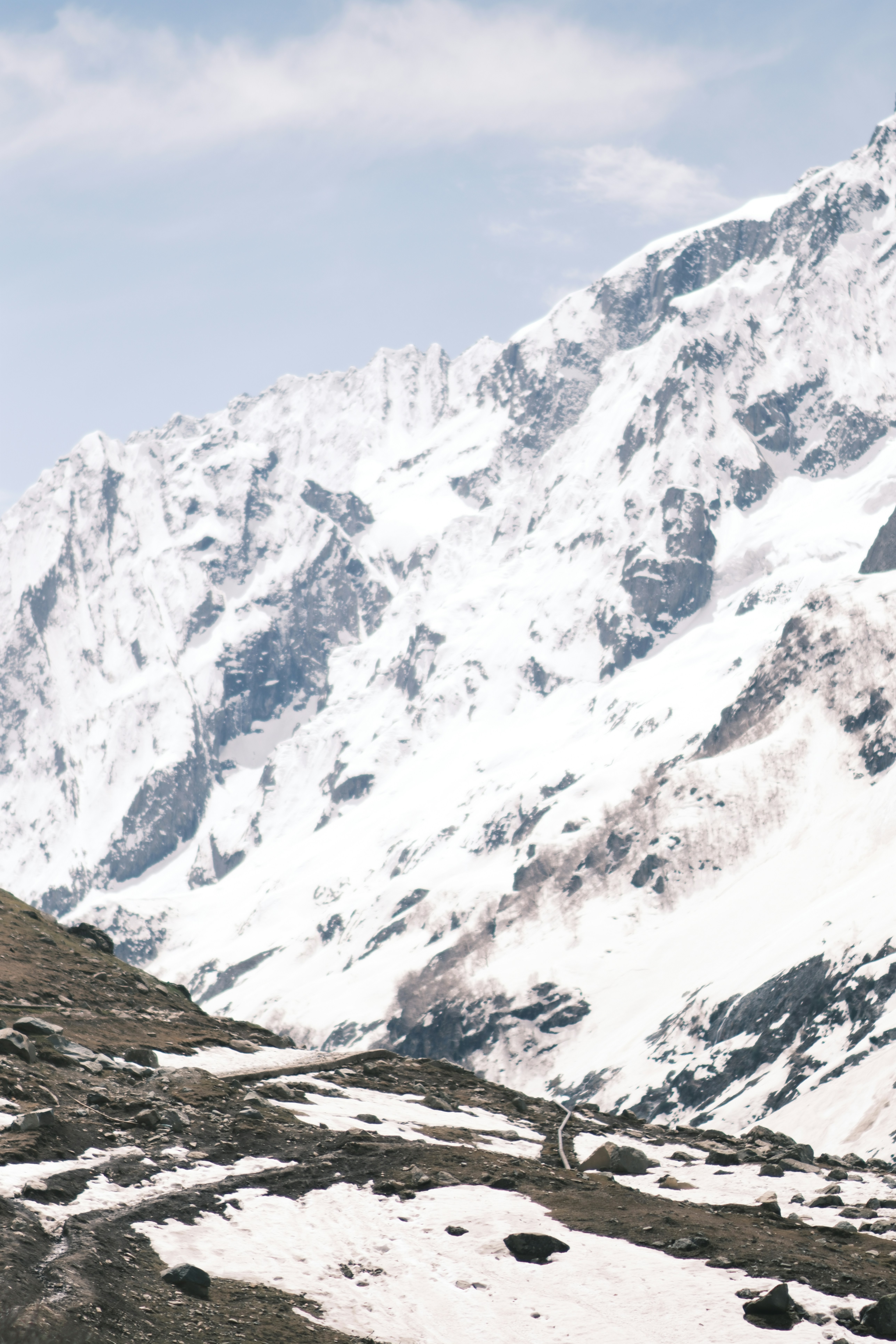 A steep snow-covered mountain slope with rocky terrain in the foreground