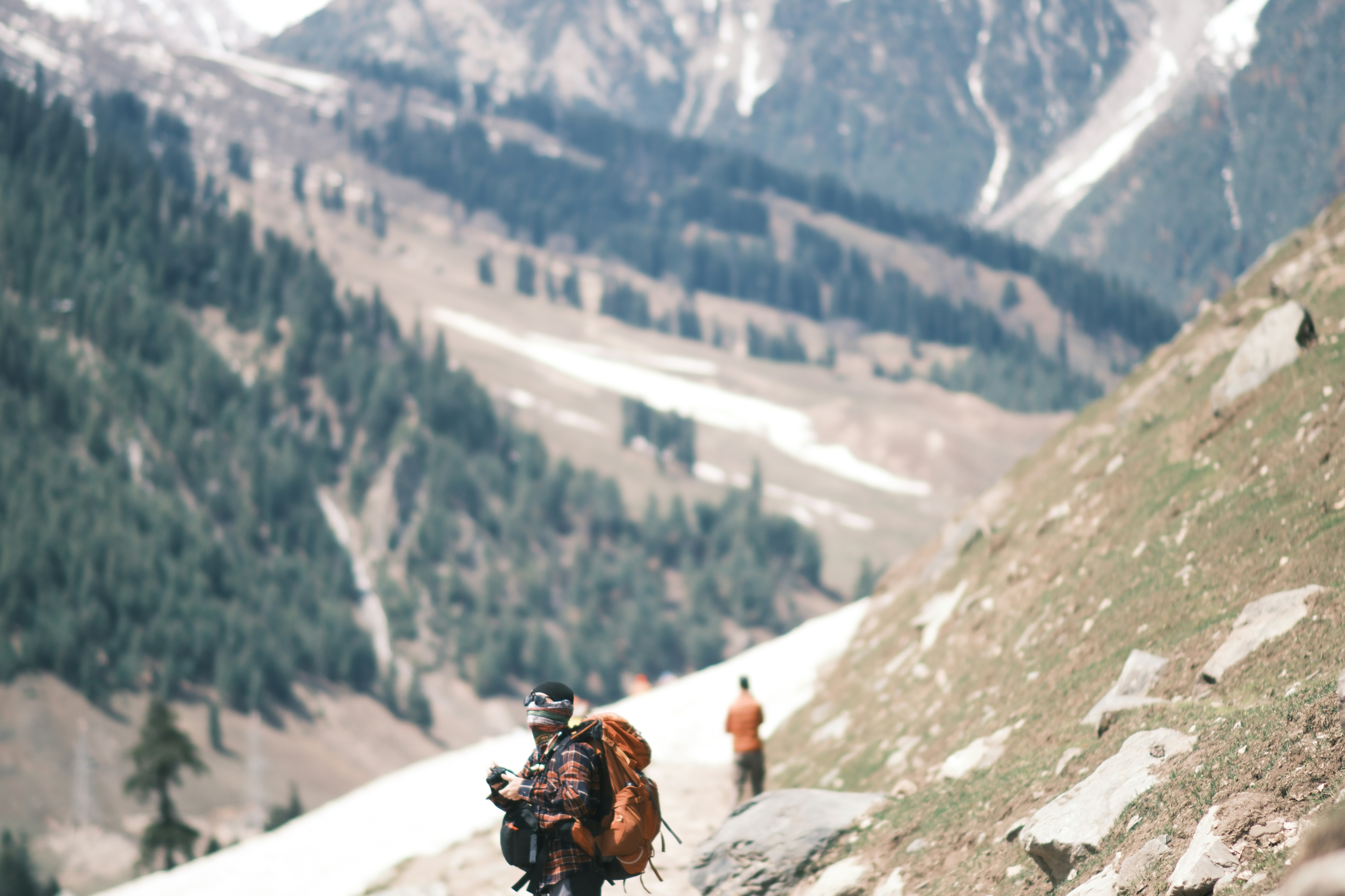 A hiker with a large backpack on a mountain trail with snow-covered slopes