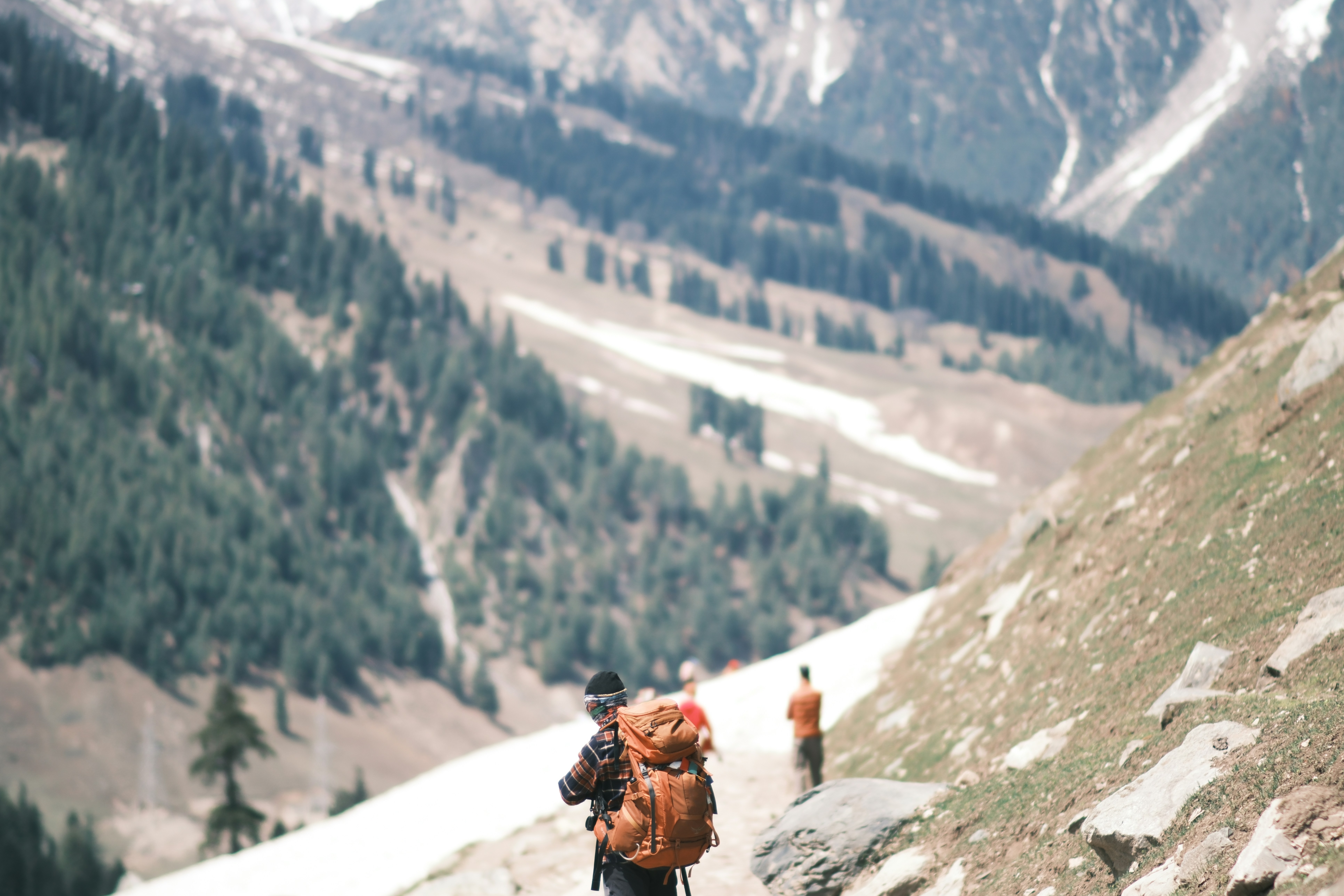 A hiker with a large orange backpack walking on a mountain trail