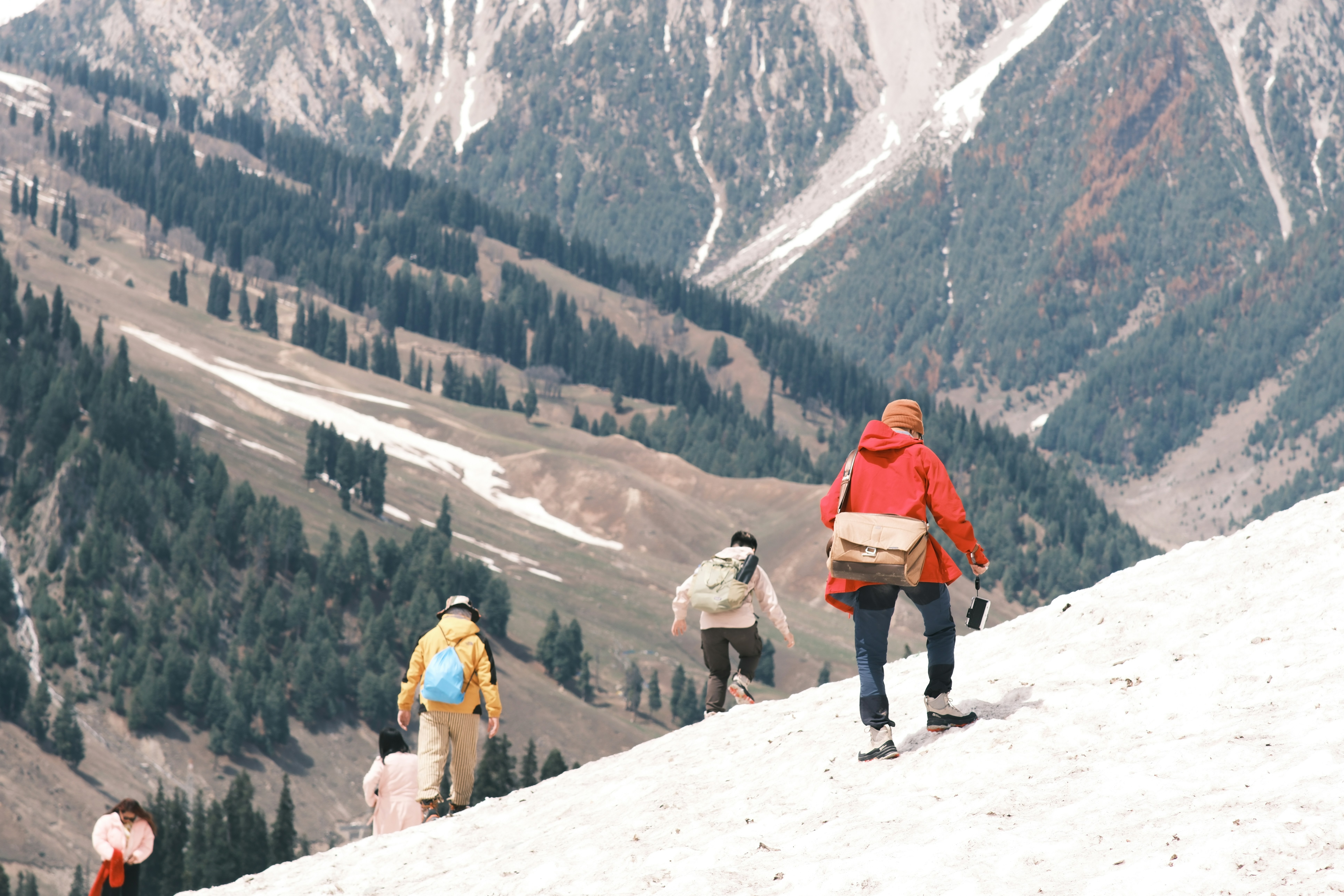 A group of people hiking up a snow-covered mountain slope in a valley