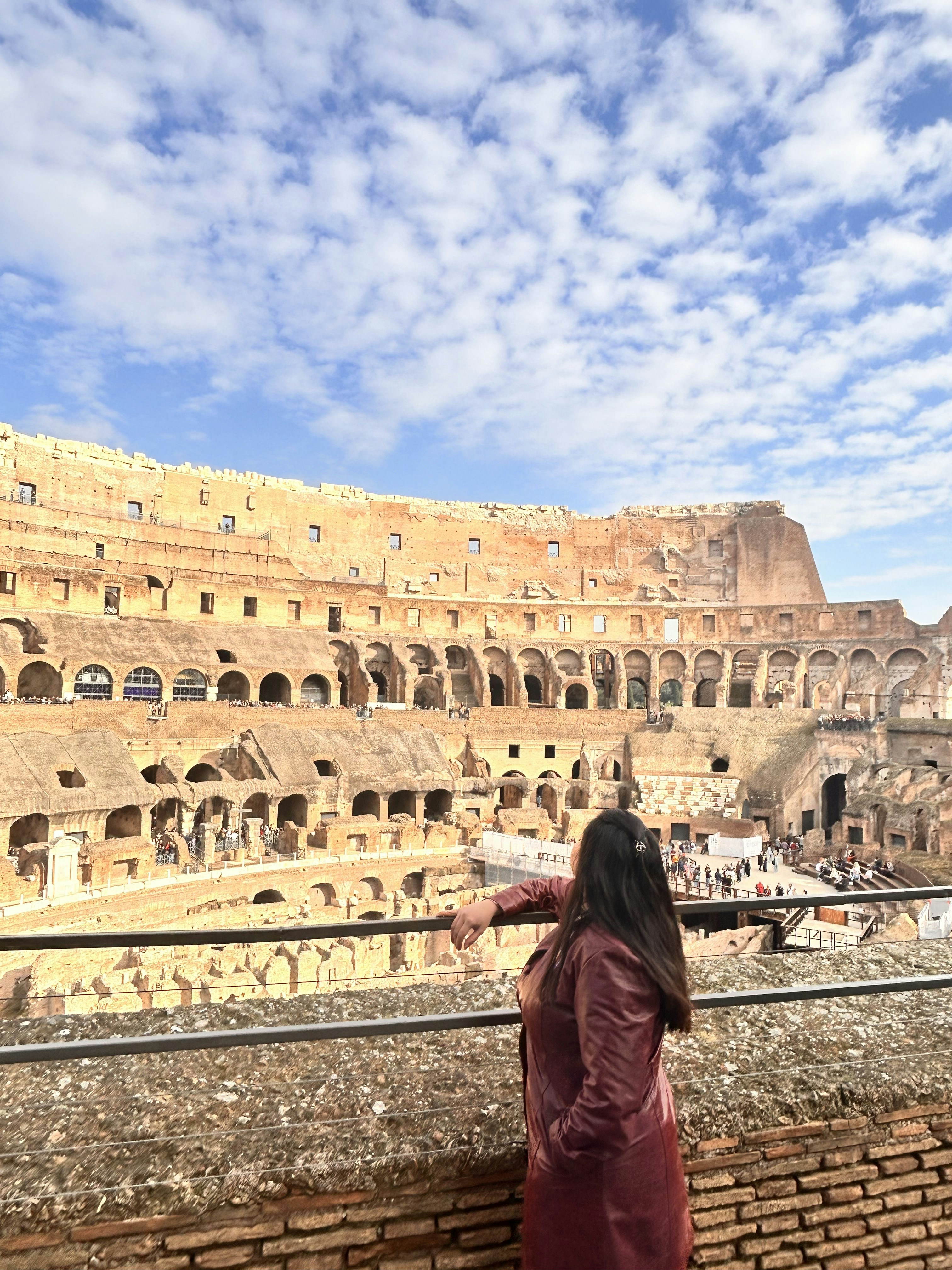 A person in a maroon jacket looking at the Colosseum in Rome