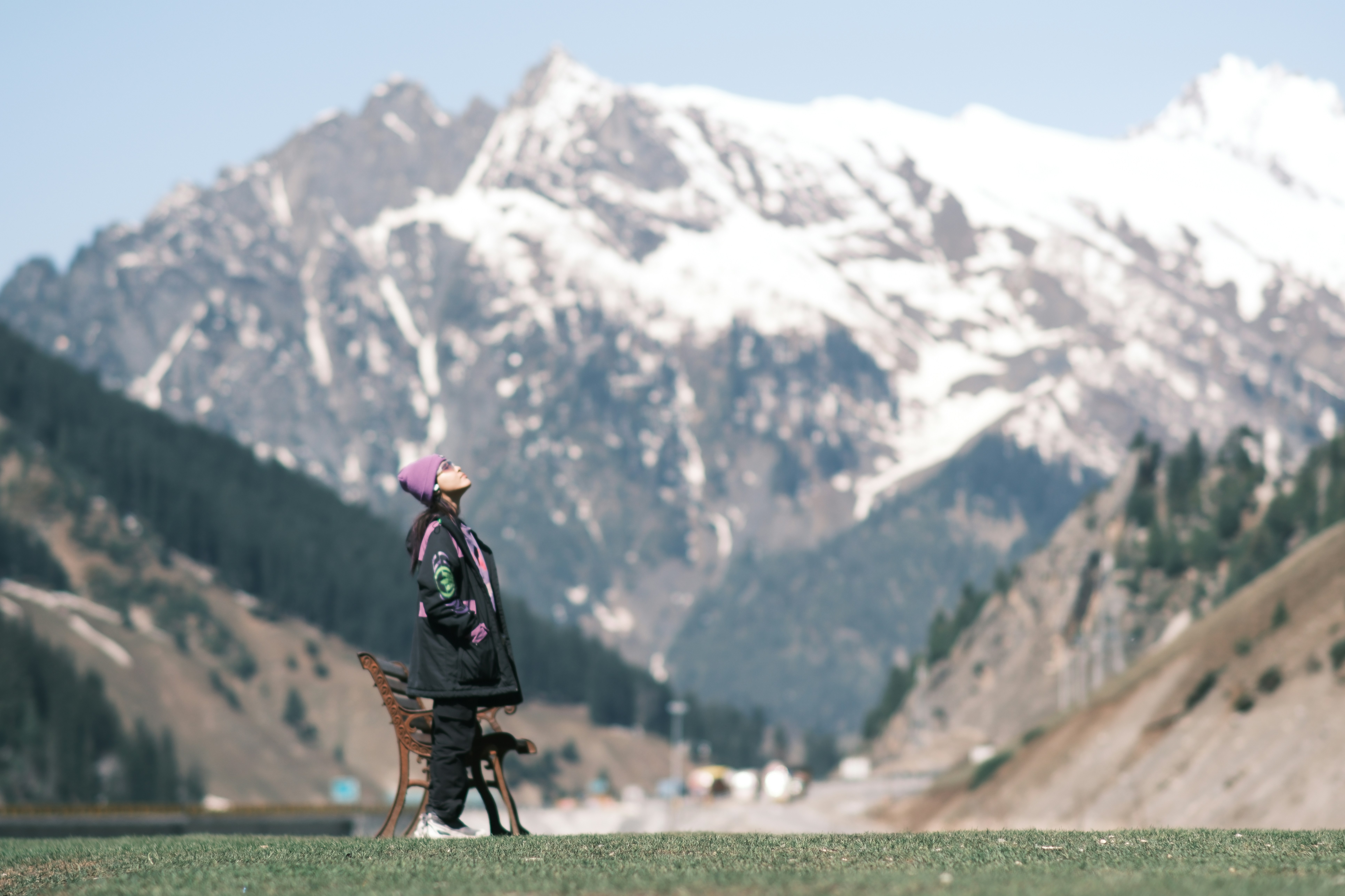A person in a purple beanie and dark jacket looking up at snowy mountains