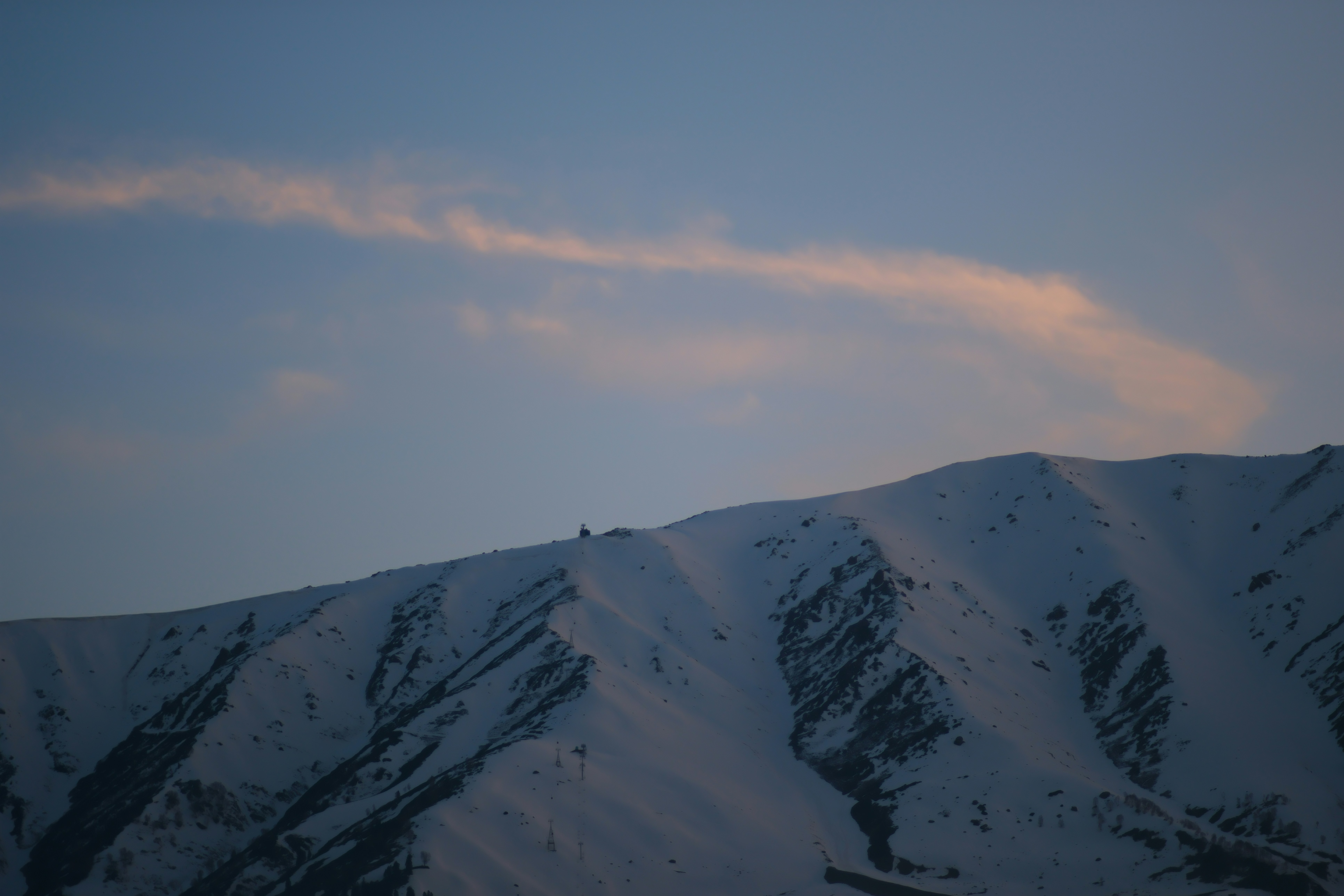 Snowy mountain peak under a pale blue sky with a thin pink cloud