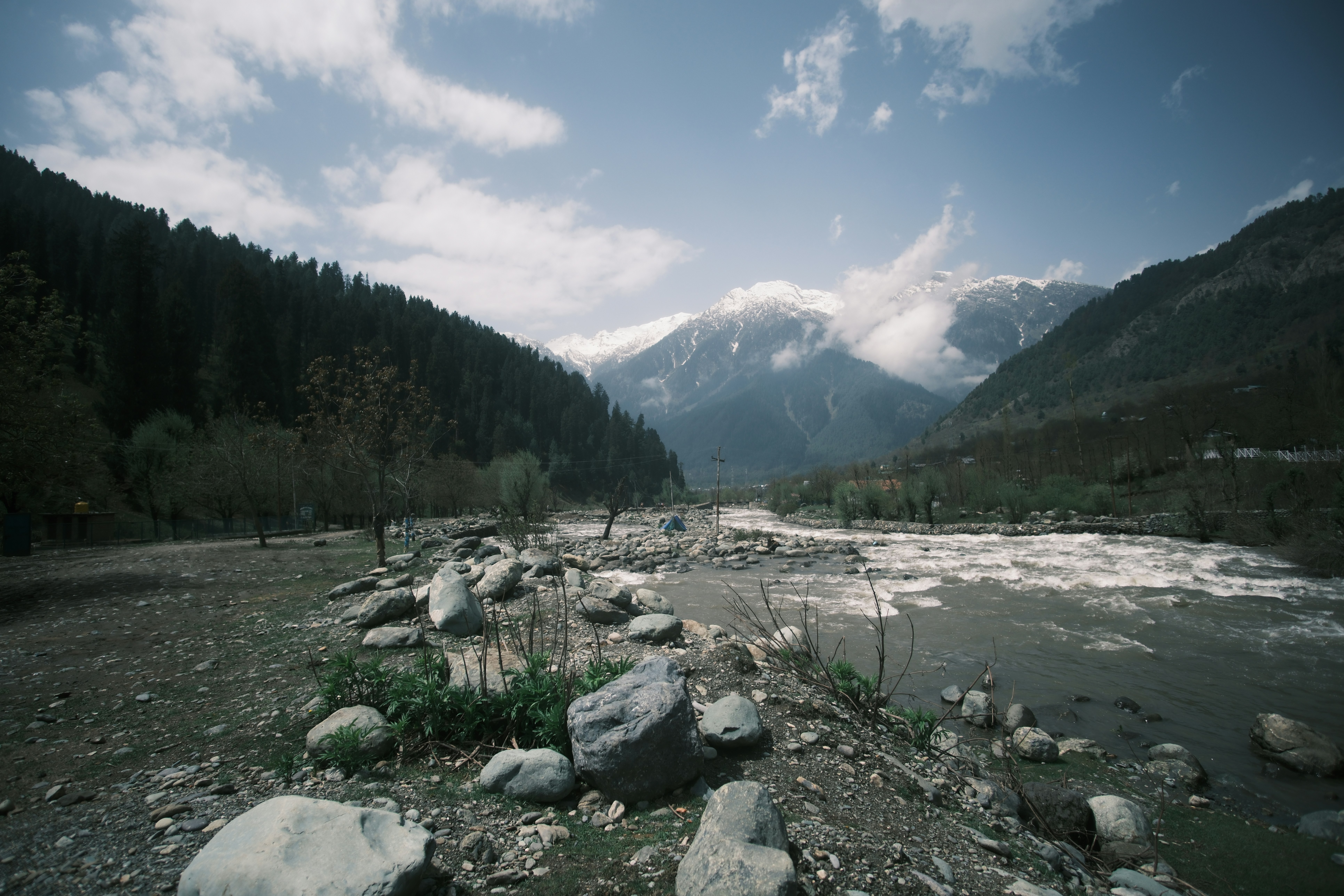 A rushing river flowing past a rocky bank toward snow-capped mountains