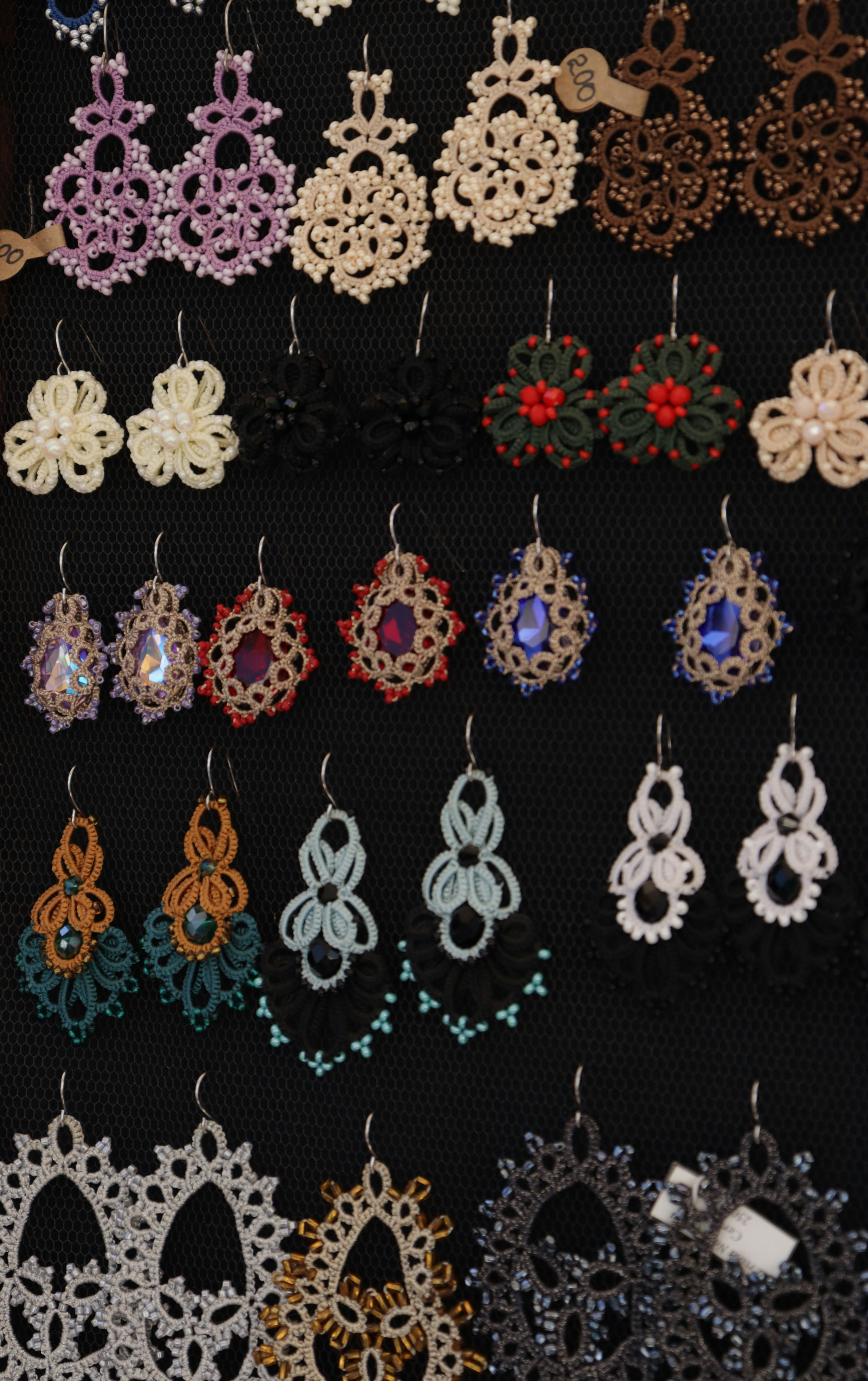 Rows of handmade tatting lace earrings in various colors displayed on a black board