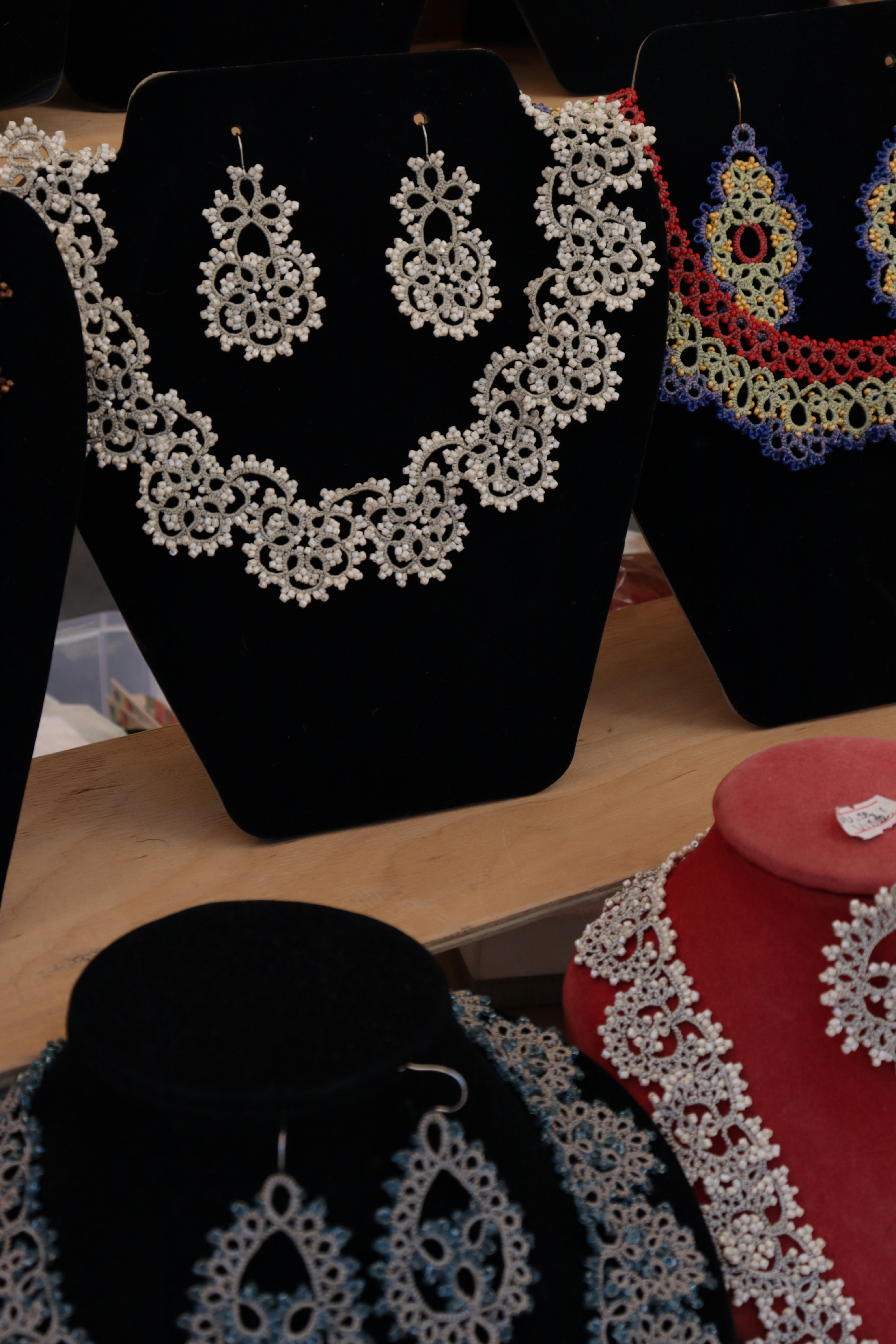 Intricate white and multicolored lace jewelry sets displayed on black and red velvet stands