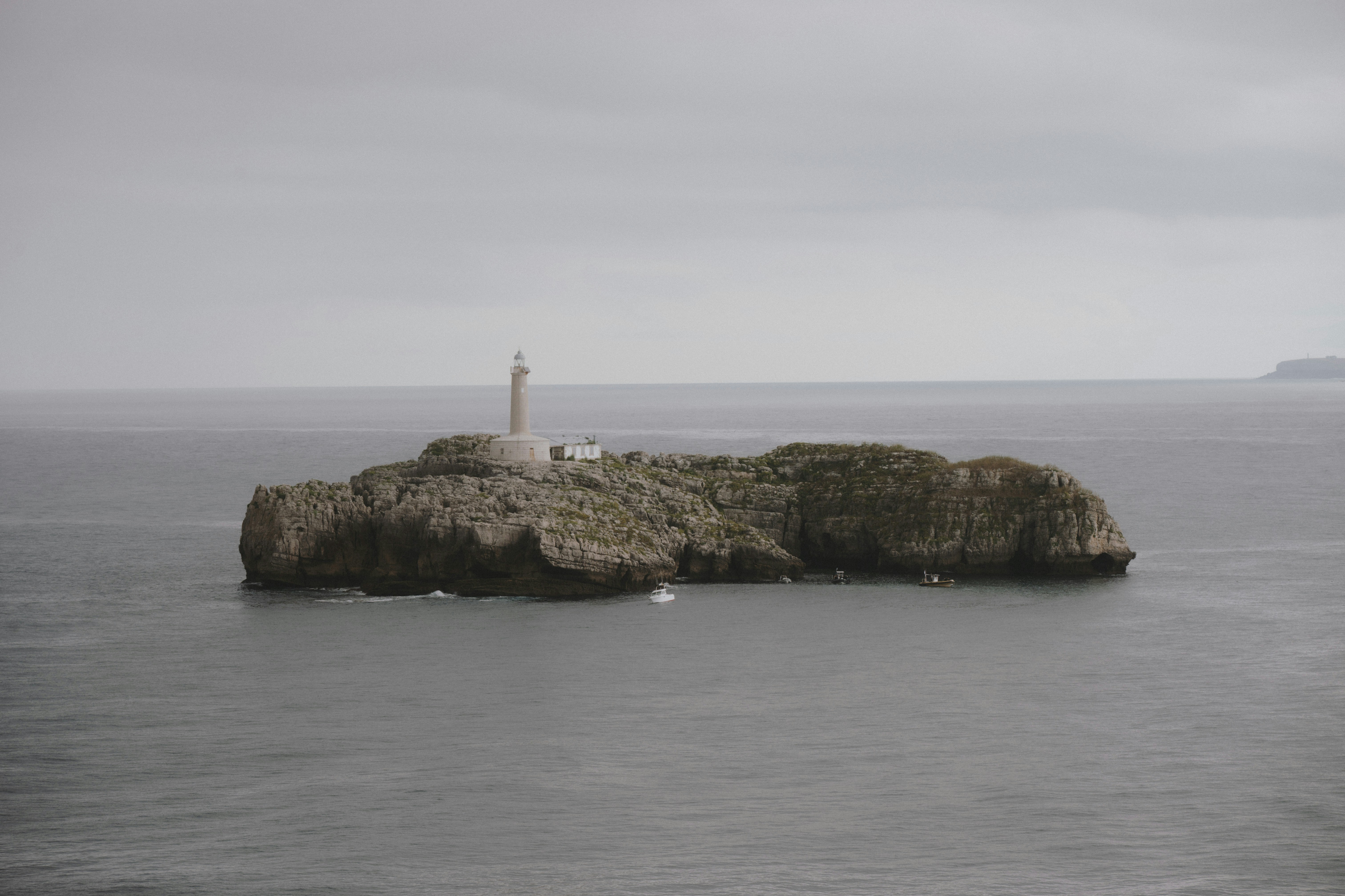 A lighthouse on a rocky island surrounded by calm grey ocean water