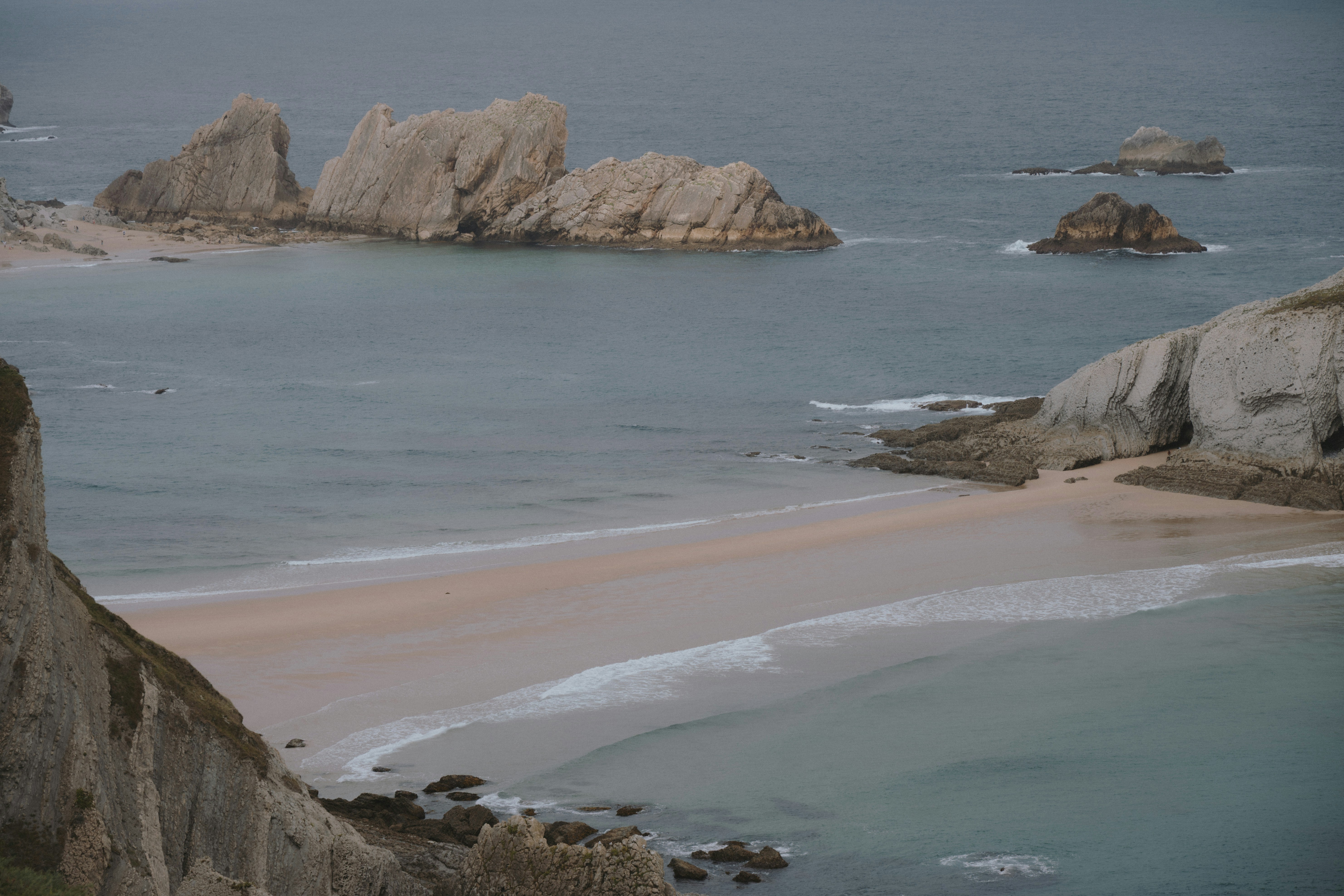 A sandy beach between rocky cliffs and sea stacks in the ocean