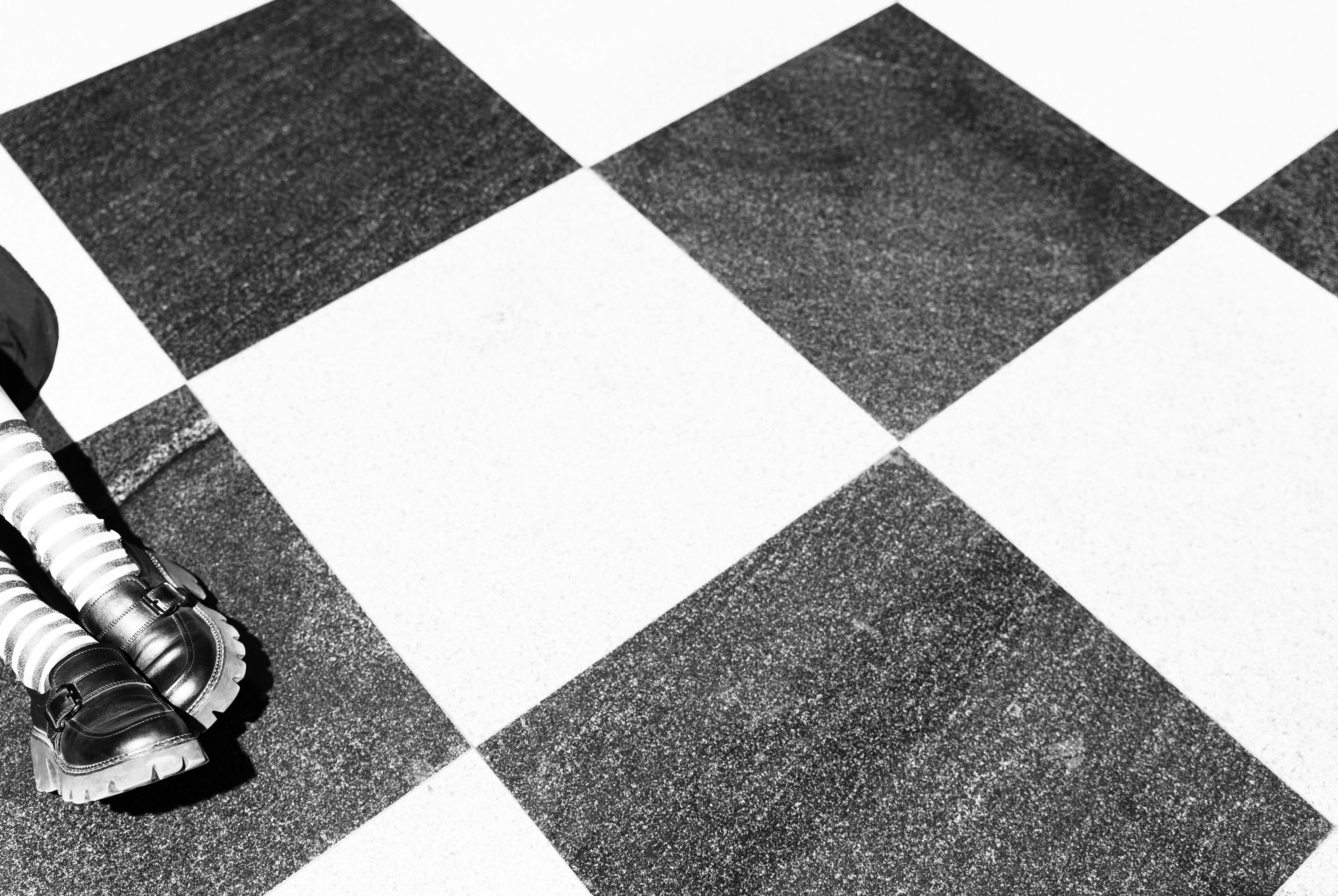 A person wearing striped socks and black shoes on a checkered floor