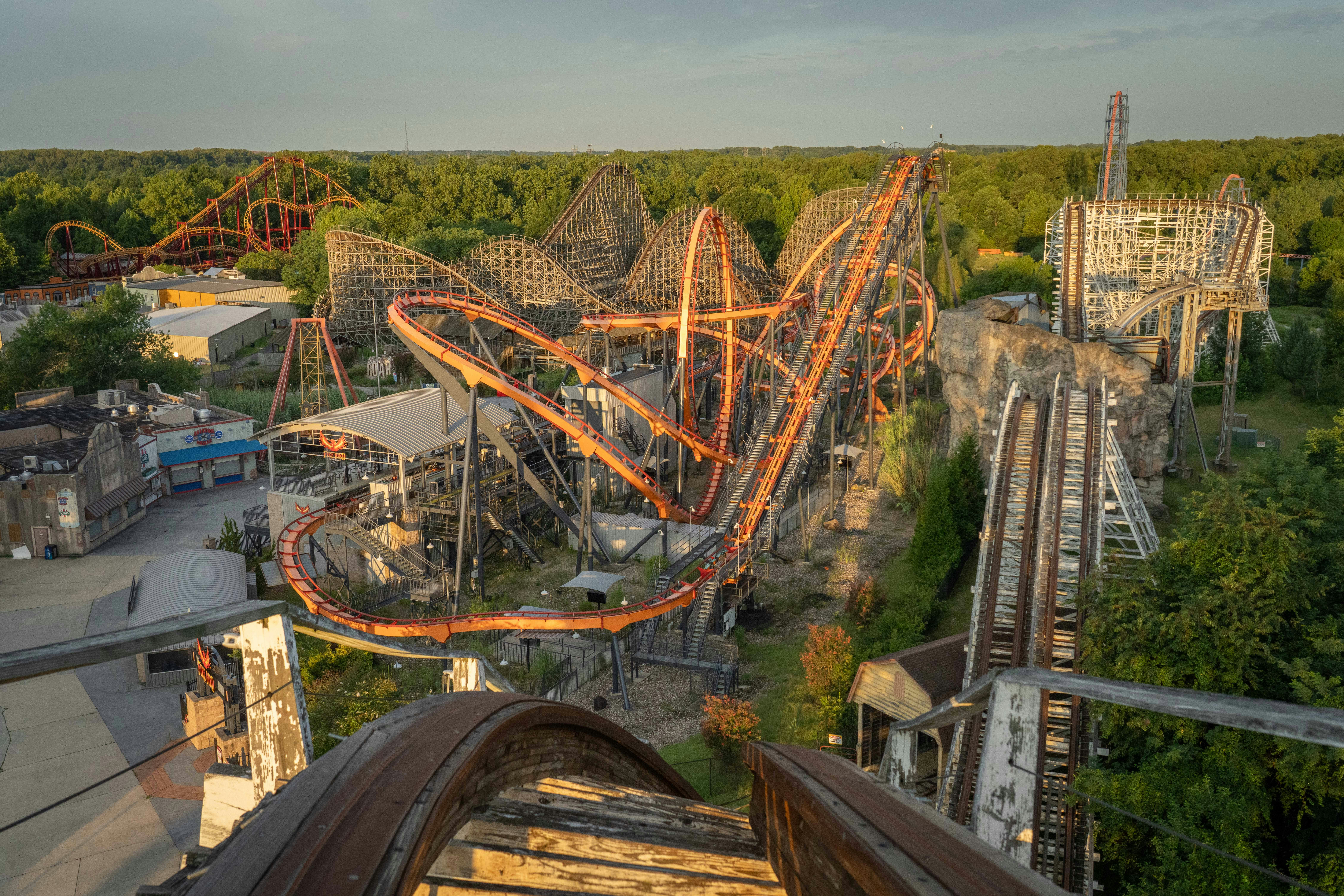 An orange steel roller coaster track winding through a wooden roller coaster structure