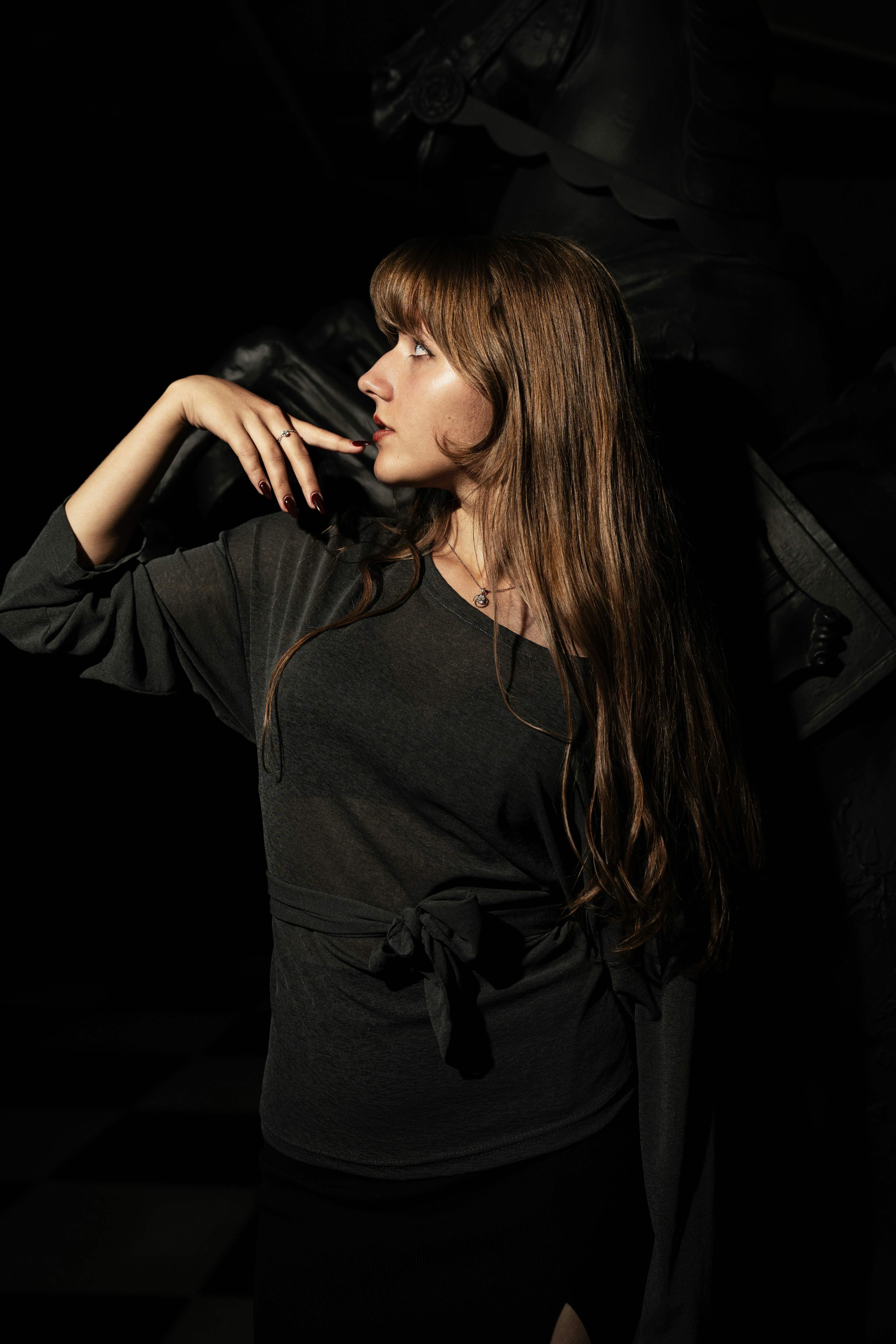 A woman with long brown hair in a dark grey top against a black background