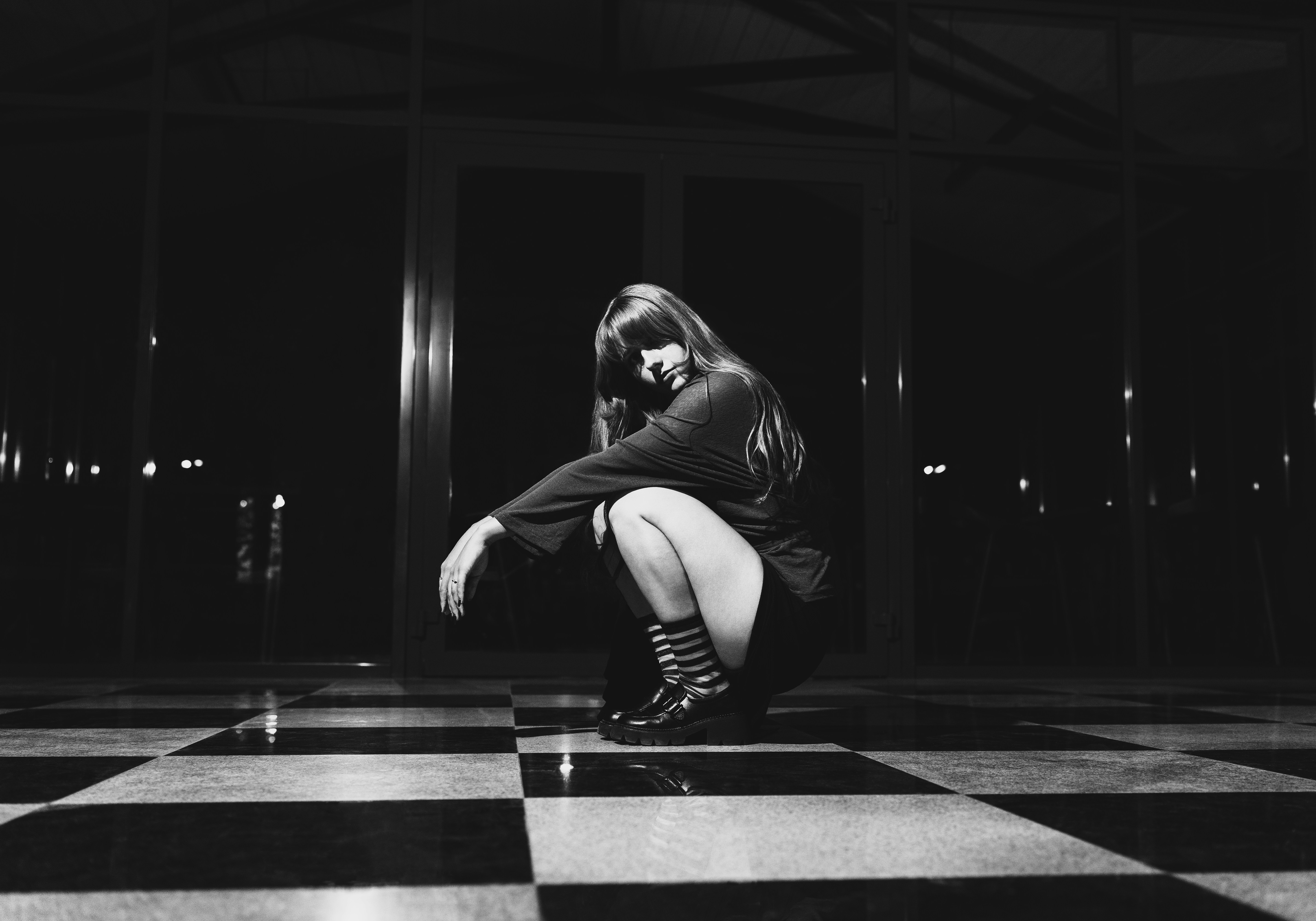 A woman crouching on a black and white checkered floor in the dark