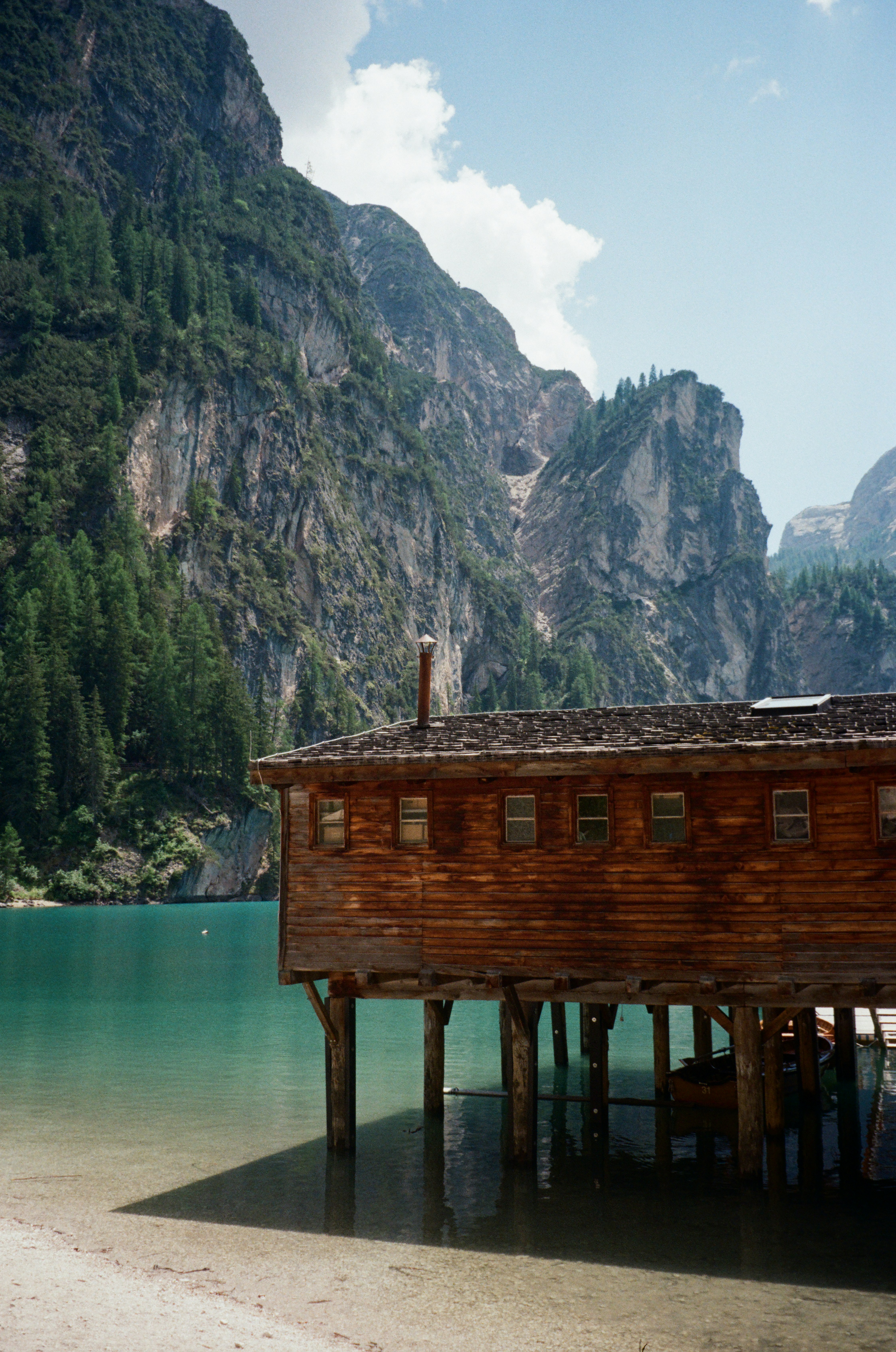 A wooden boathouse on stilts over turquoise water beneath towering rocky mountain cliffs