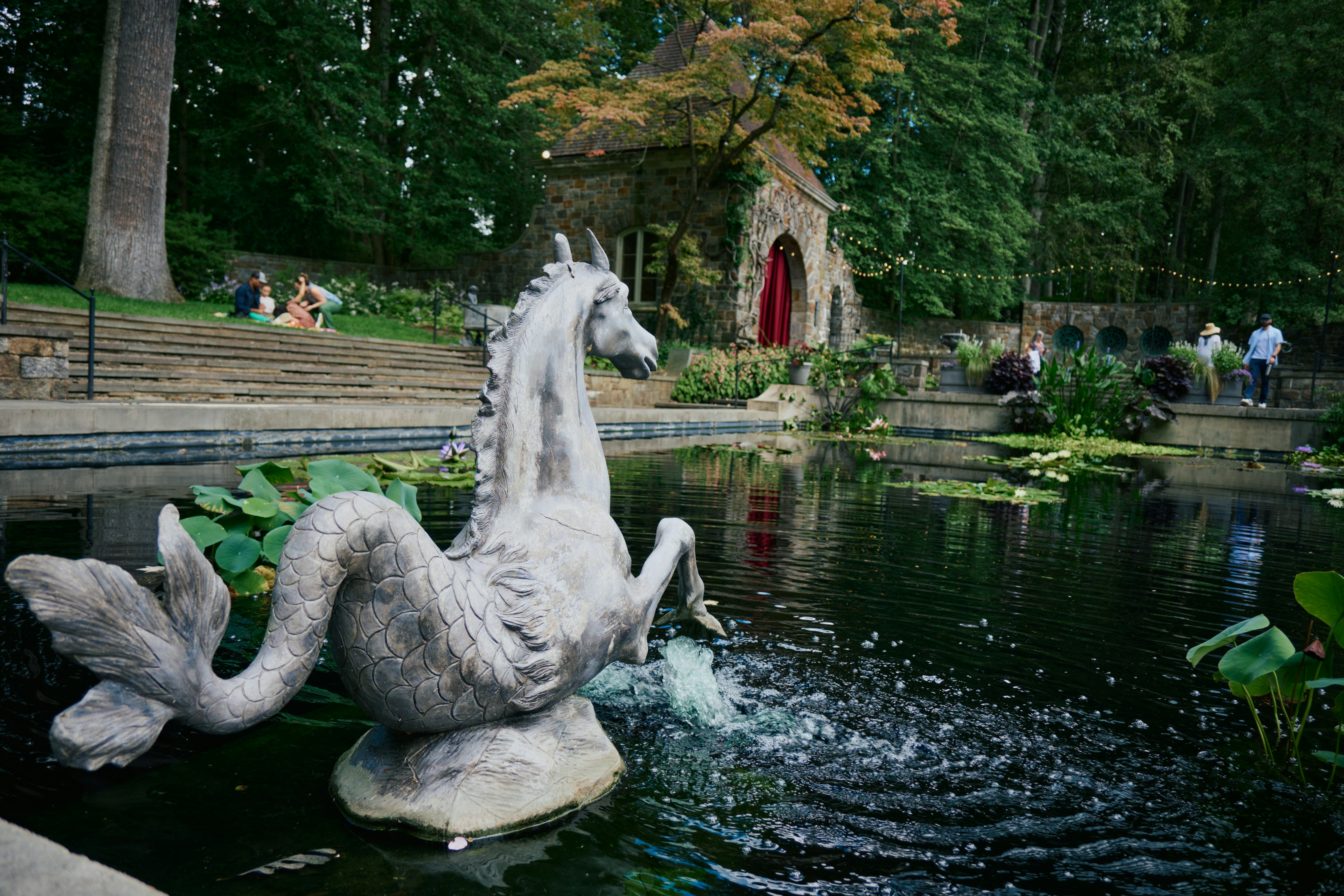 A stone hippocampus fountain in a pond with people on a grassy bank