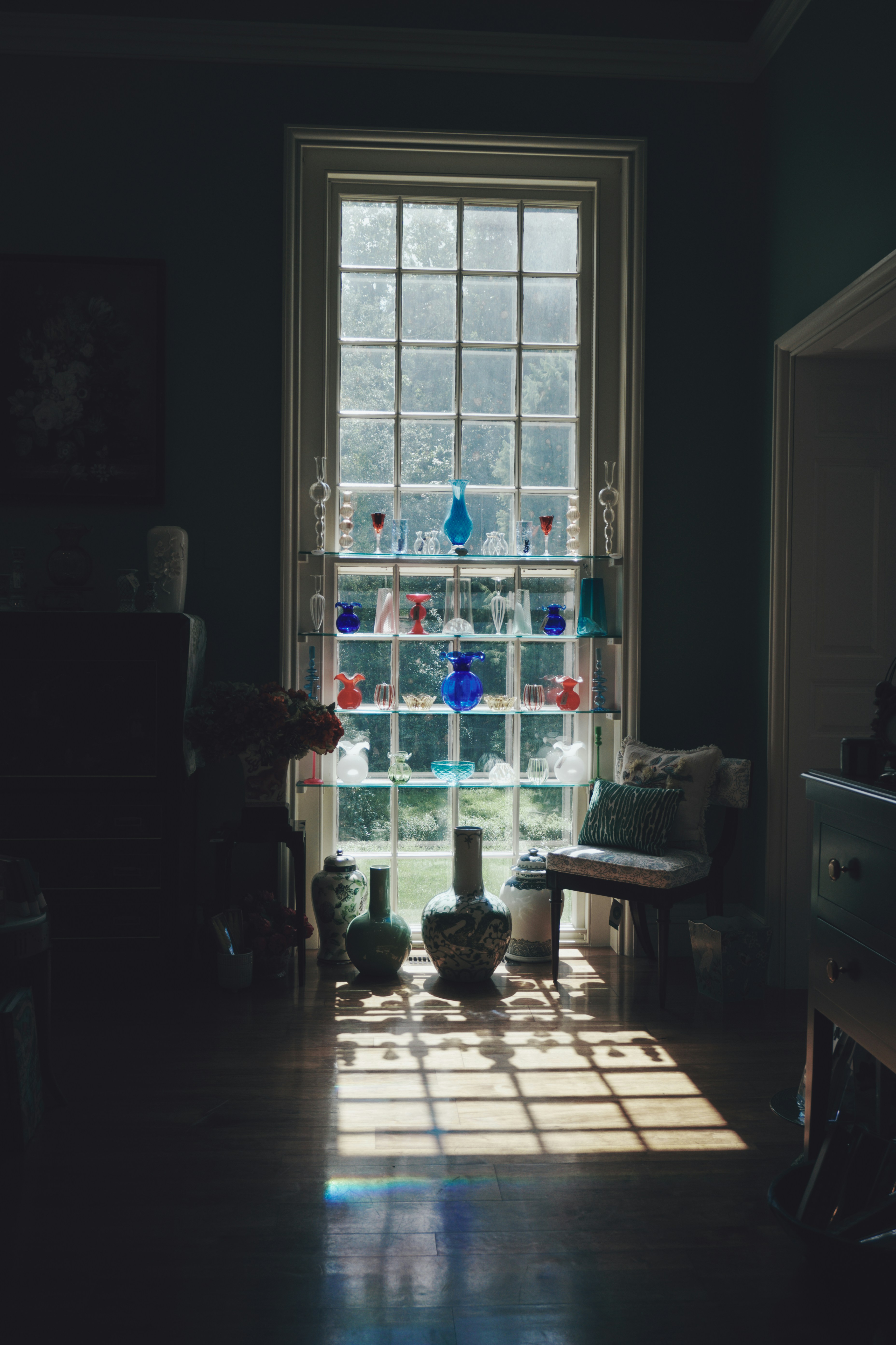 Glass vases on shelves in a window casting shadows on a wooden floor