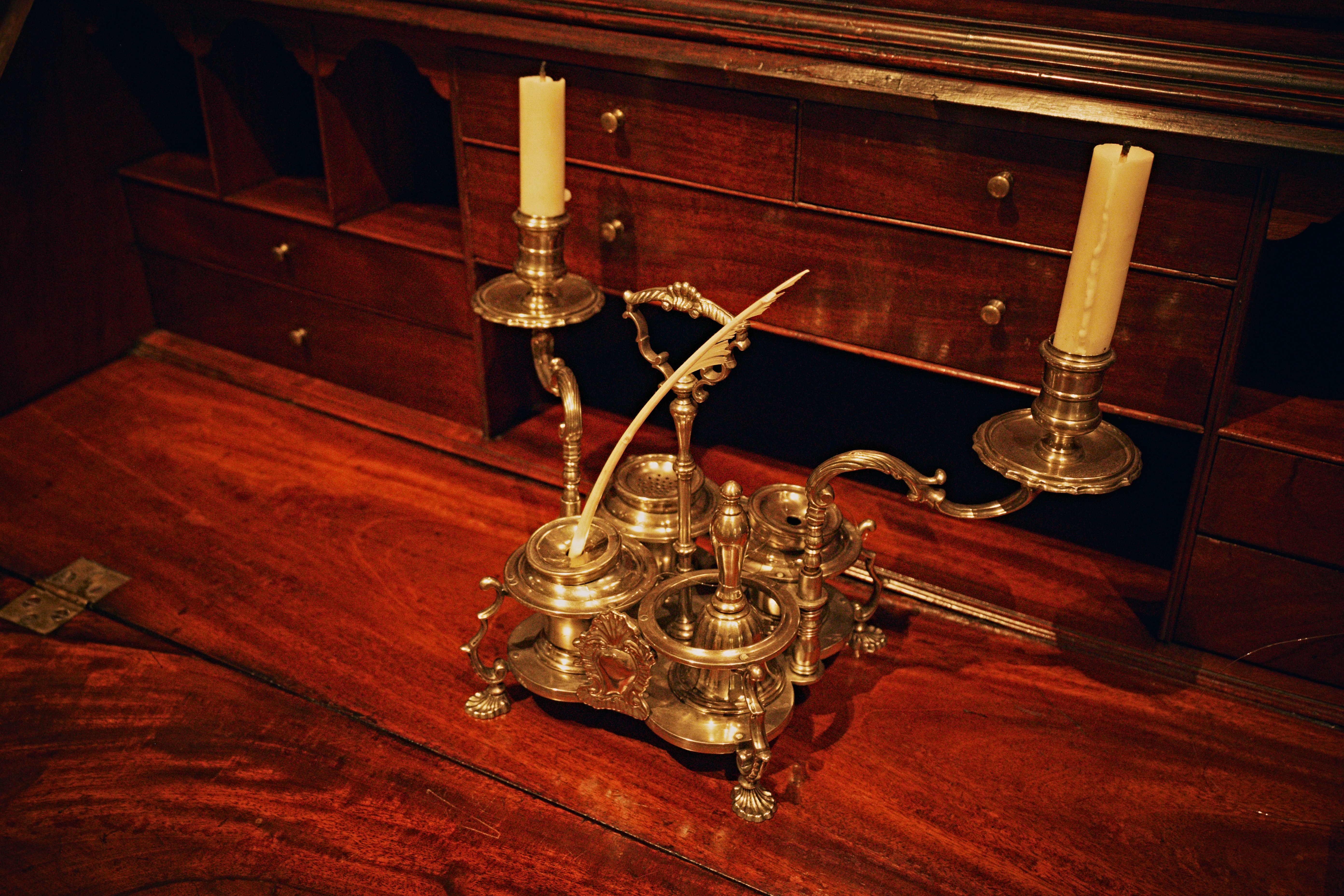 A brass inkwell set with two candles and a quill on a wooden desk