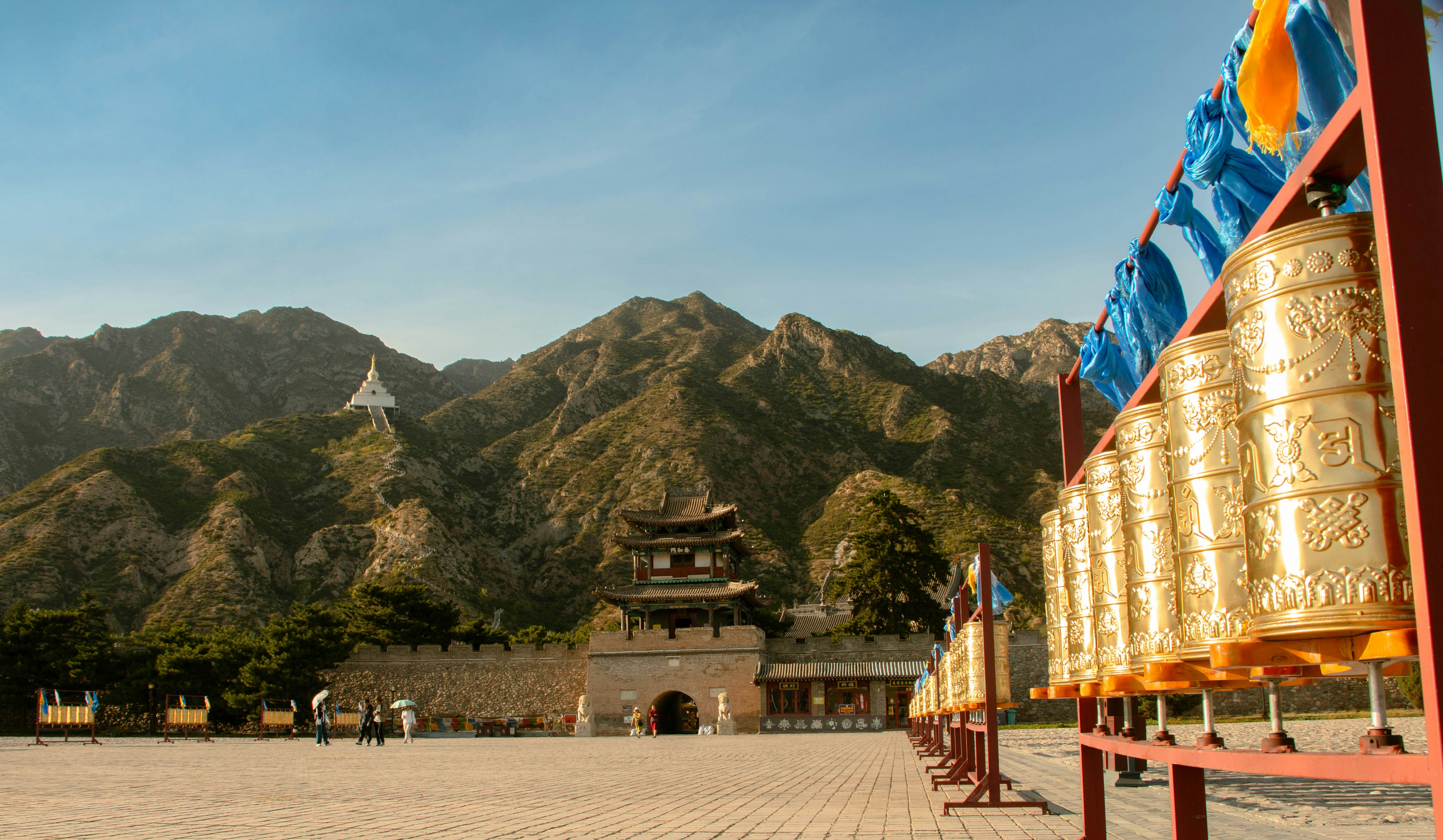 Golden prayer wheels in the foreground of a temple complex with mountain backdrop