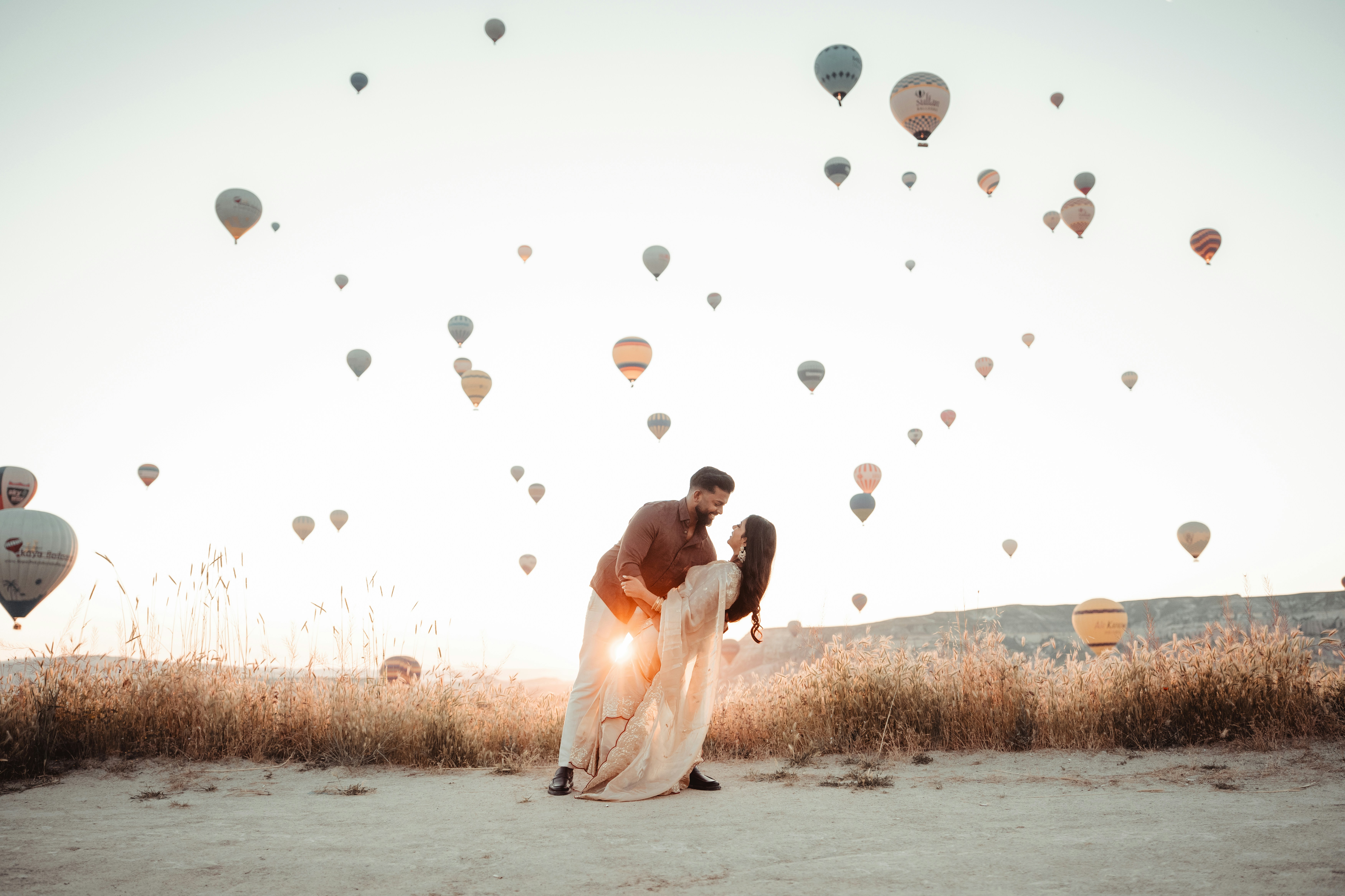 A couple in traditional clothing dancing in a field with hot air balloons above