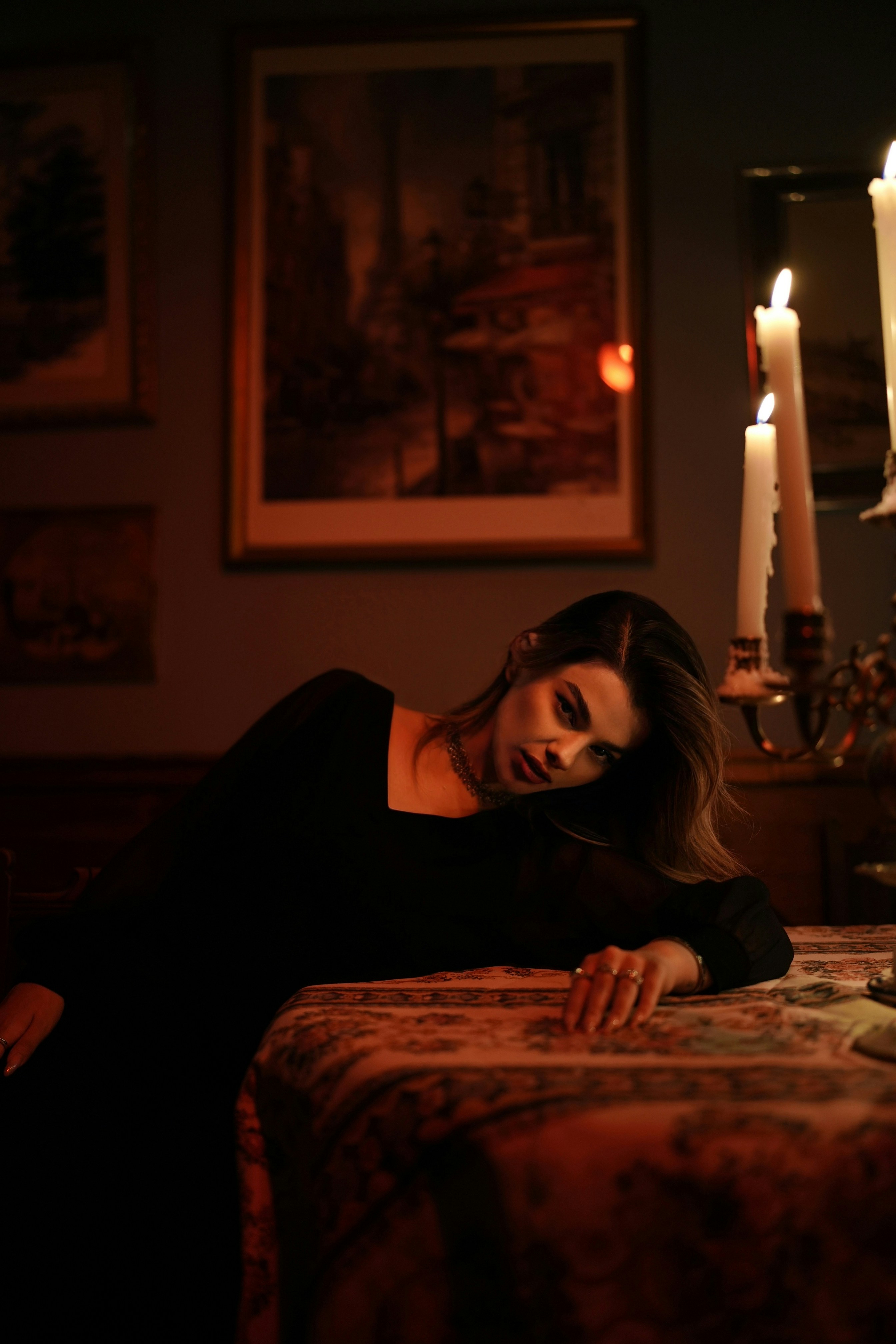 A woman in a black dress leaning on a table by candlelight