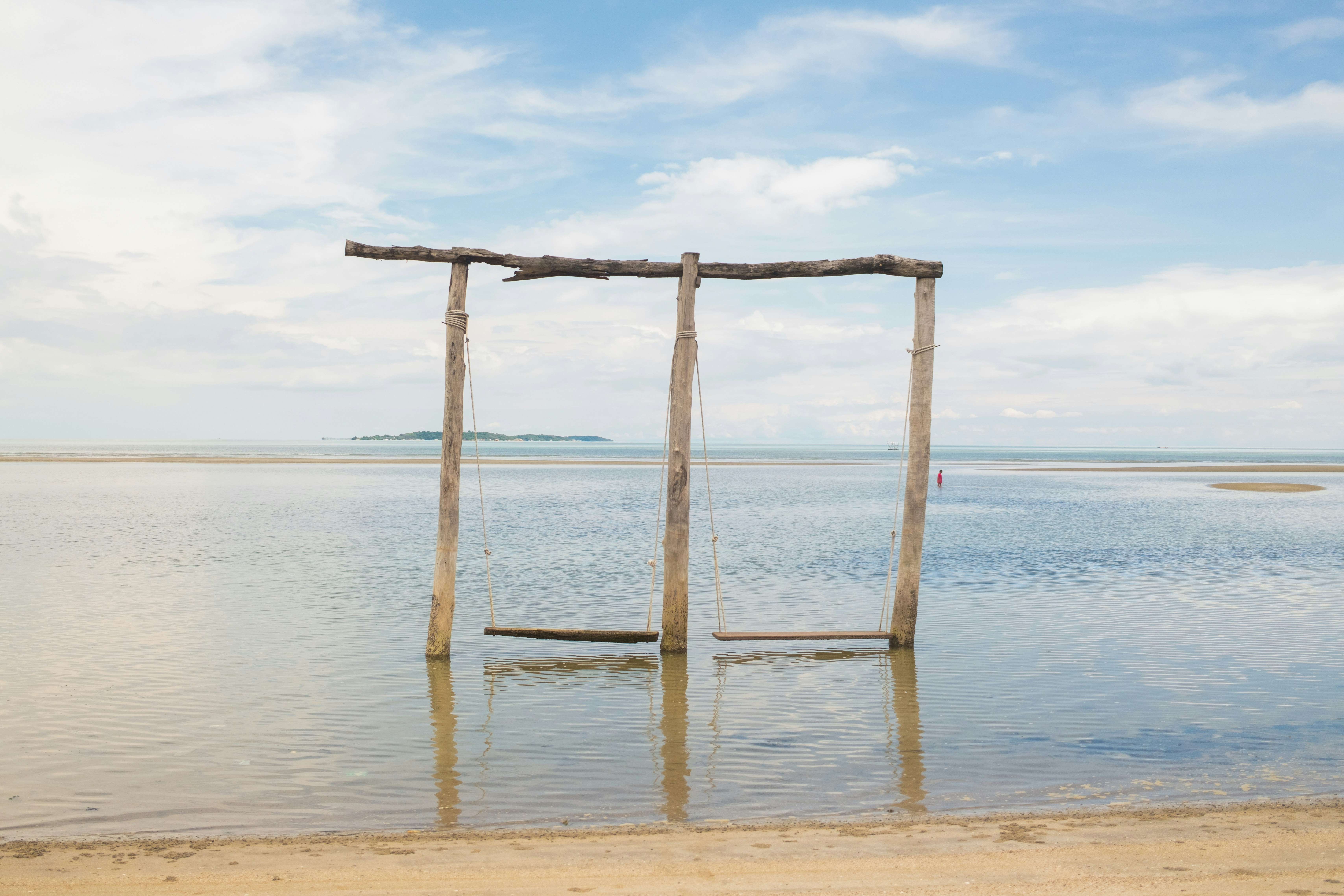 Two wooden swings hanging from a frame in shallow ocean water