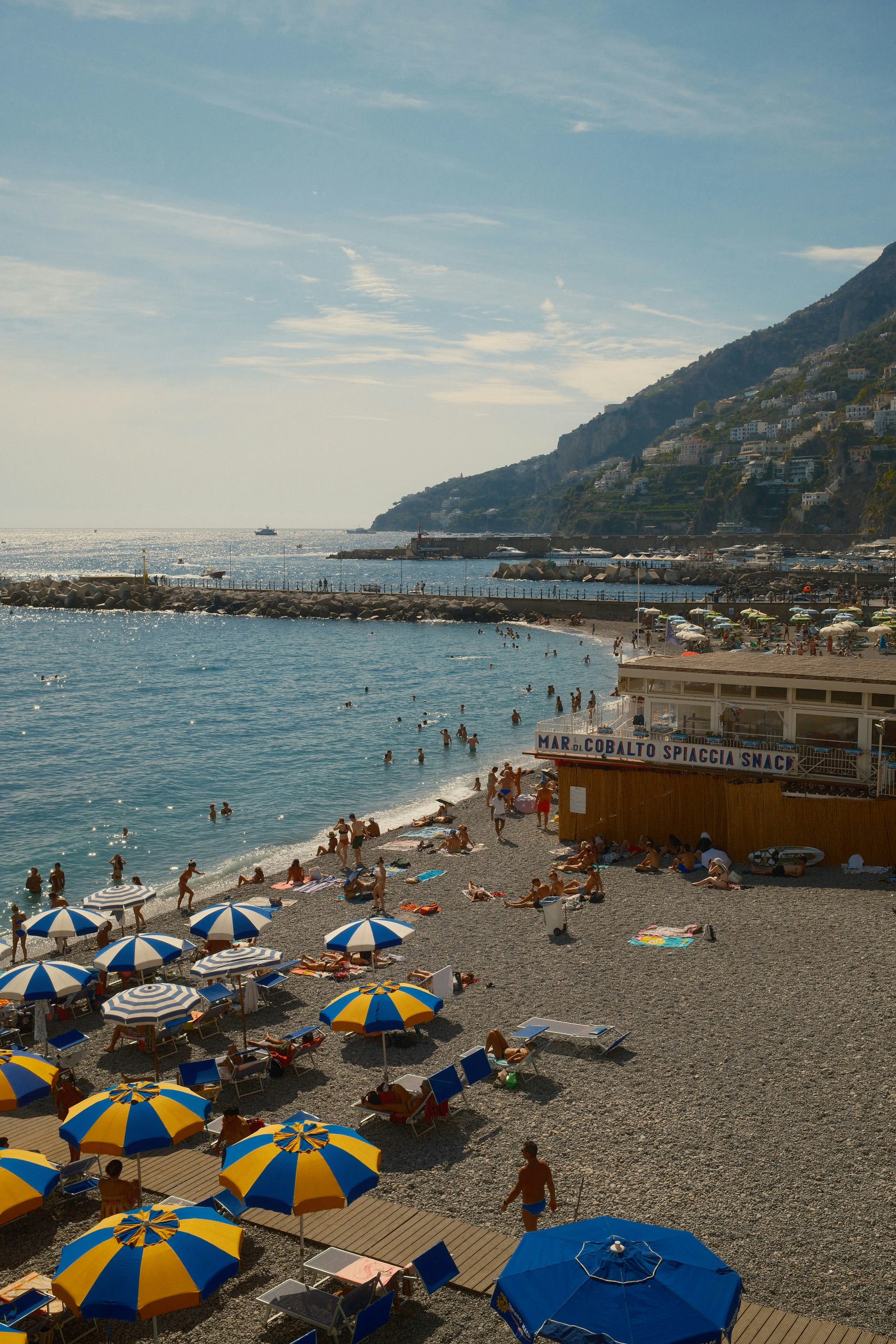 People on a pebble beach with blue and yellow umbrellas in Positano, Italy