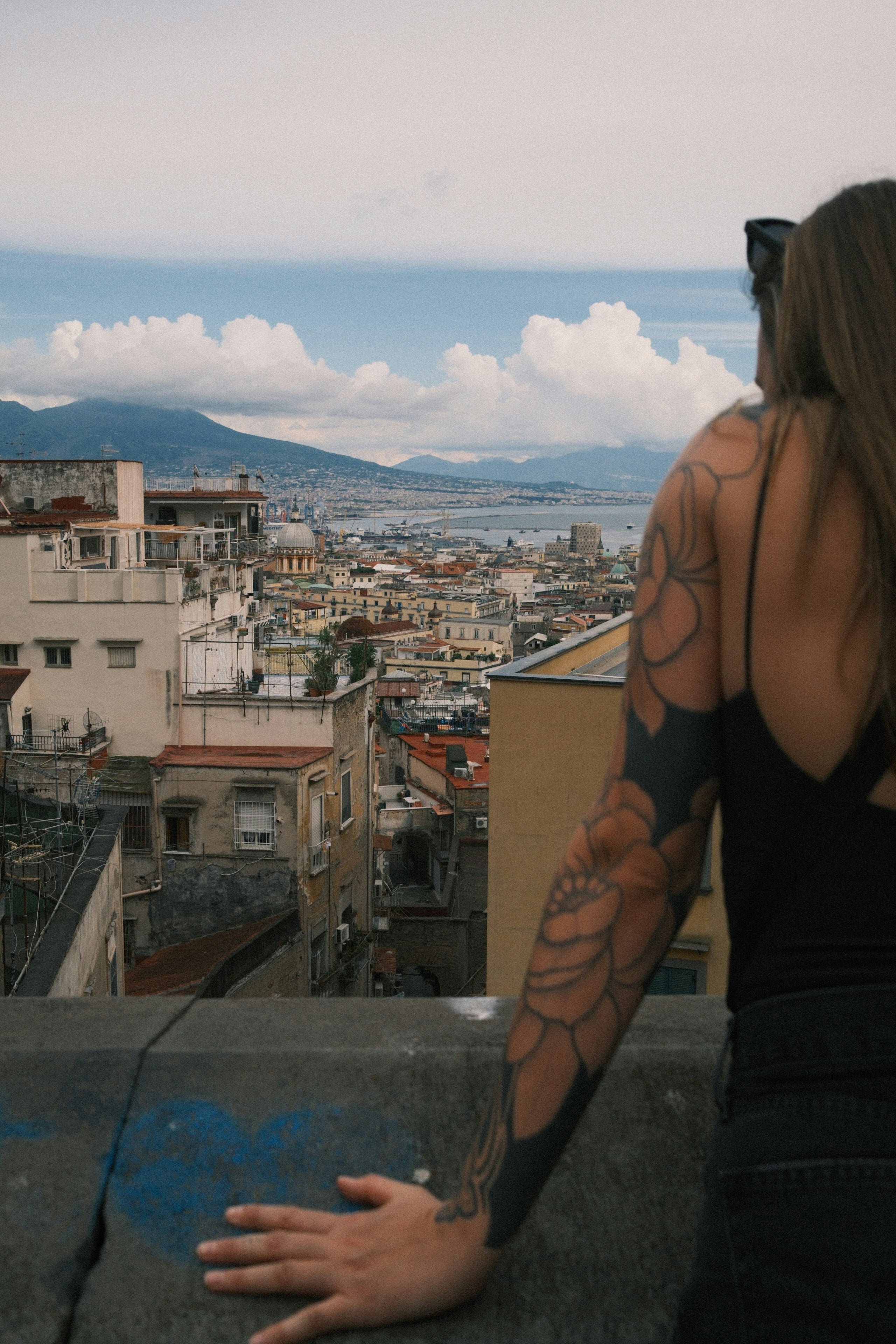 A person with a floral arm tattoo overlooking the city of Naples, Italy