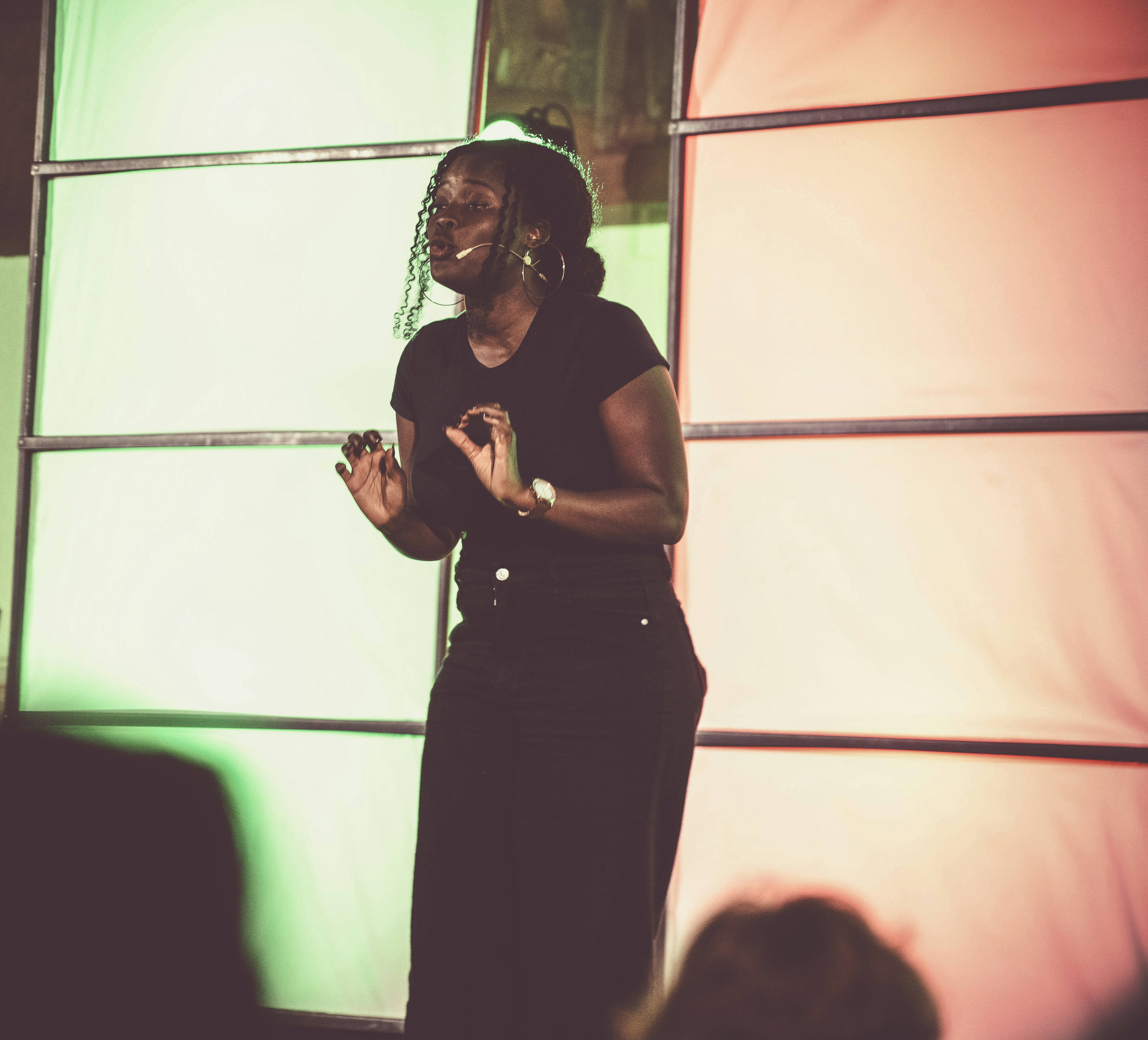 A woman in a black t-shirt speaking on stage before a colorful backdrop