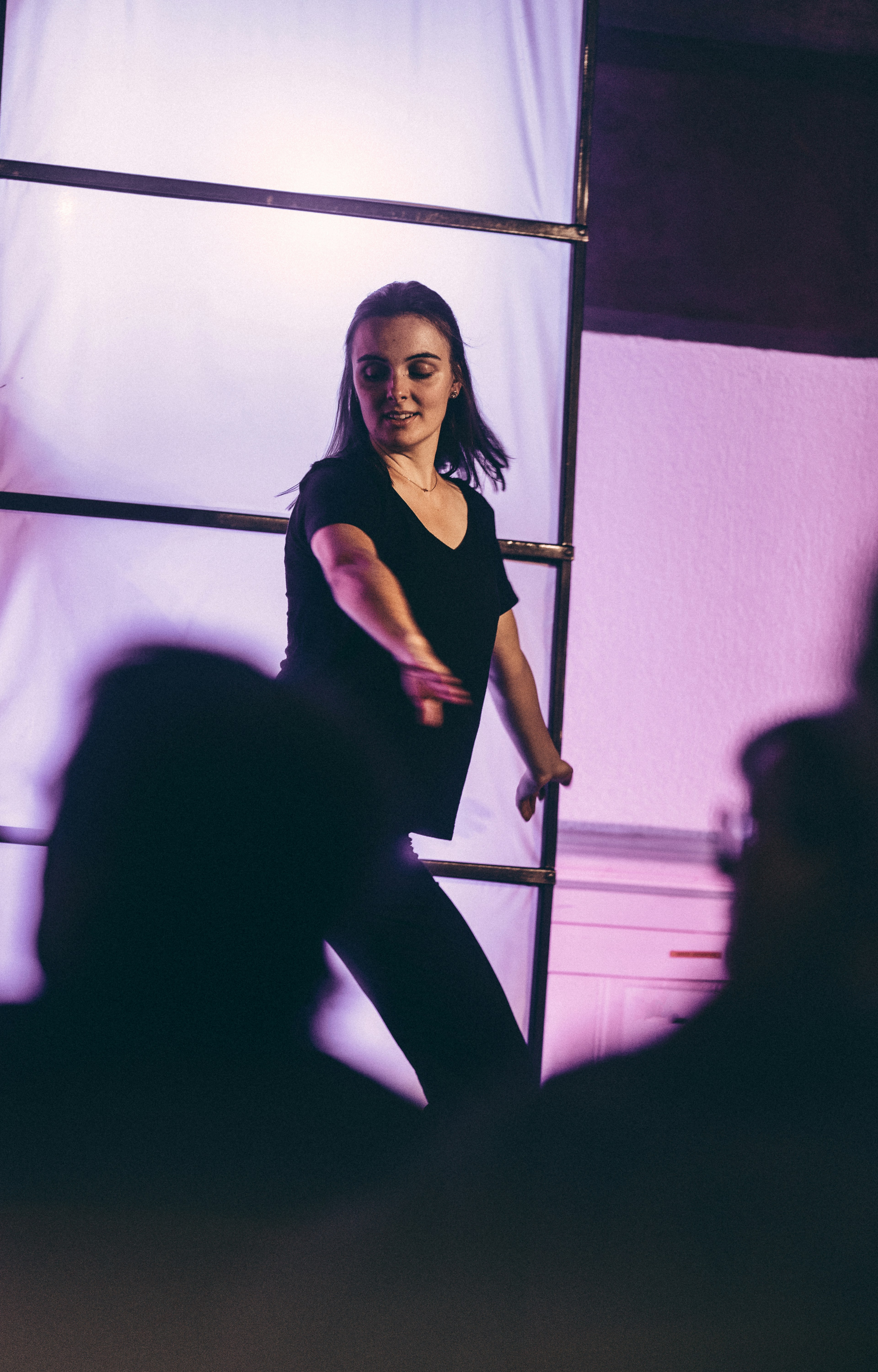 A woman in a black t-shirt dancing before a backlit screen in purple light