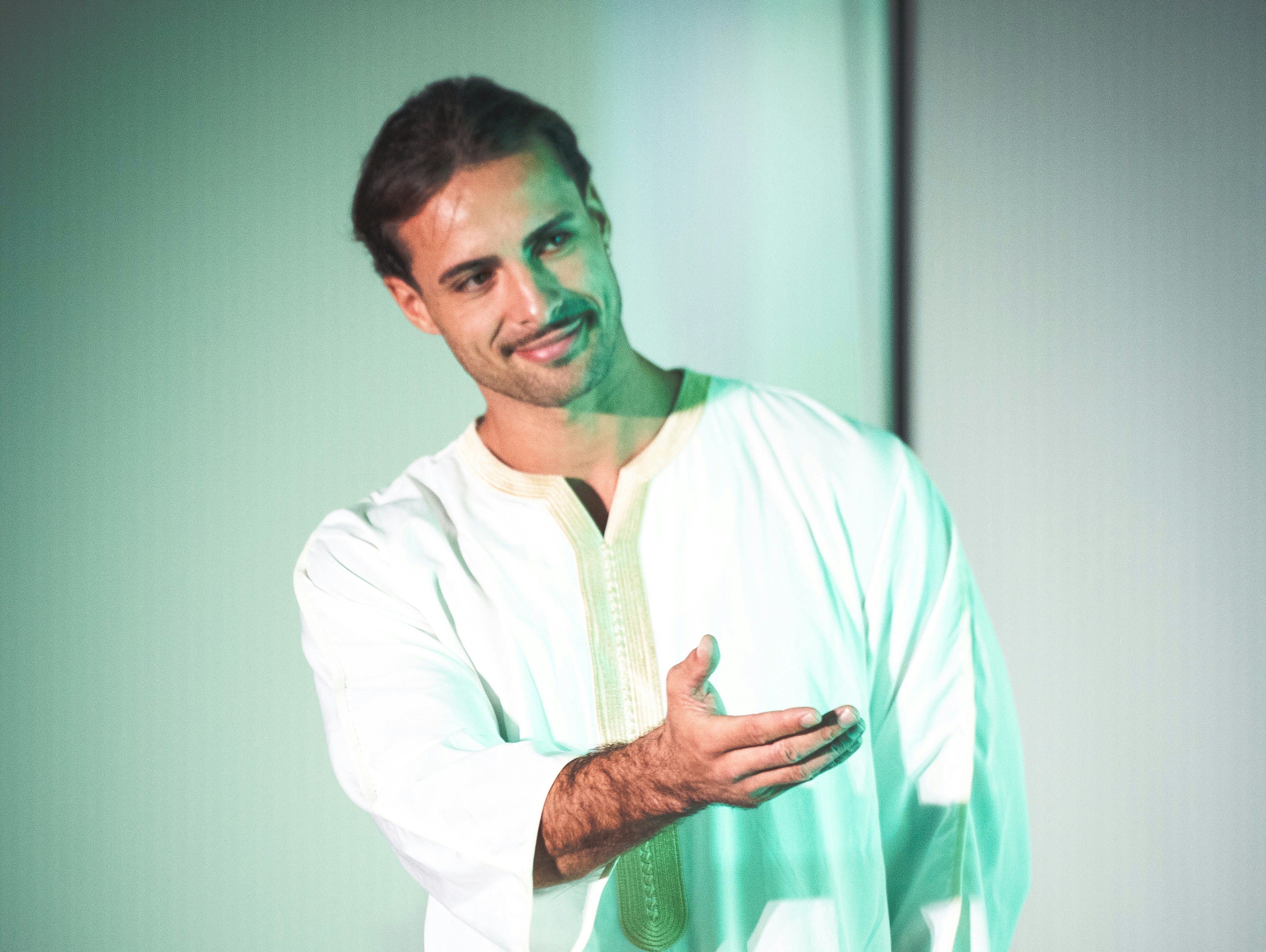 A man in a white tunic with gold embroidery gesturing with his hand