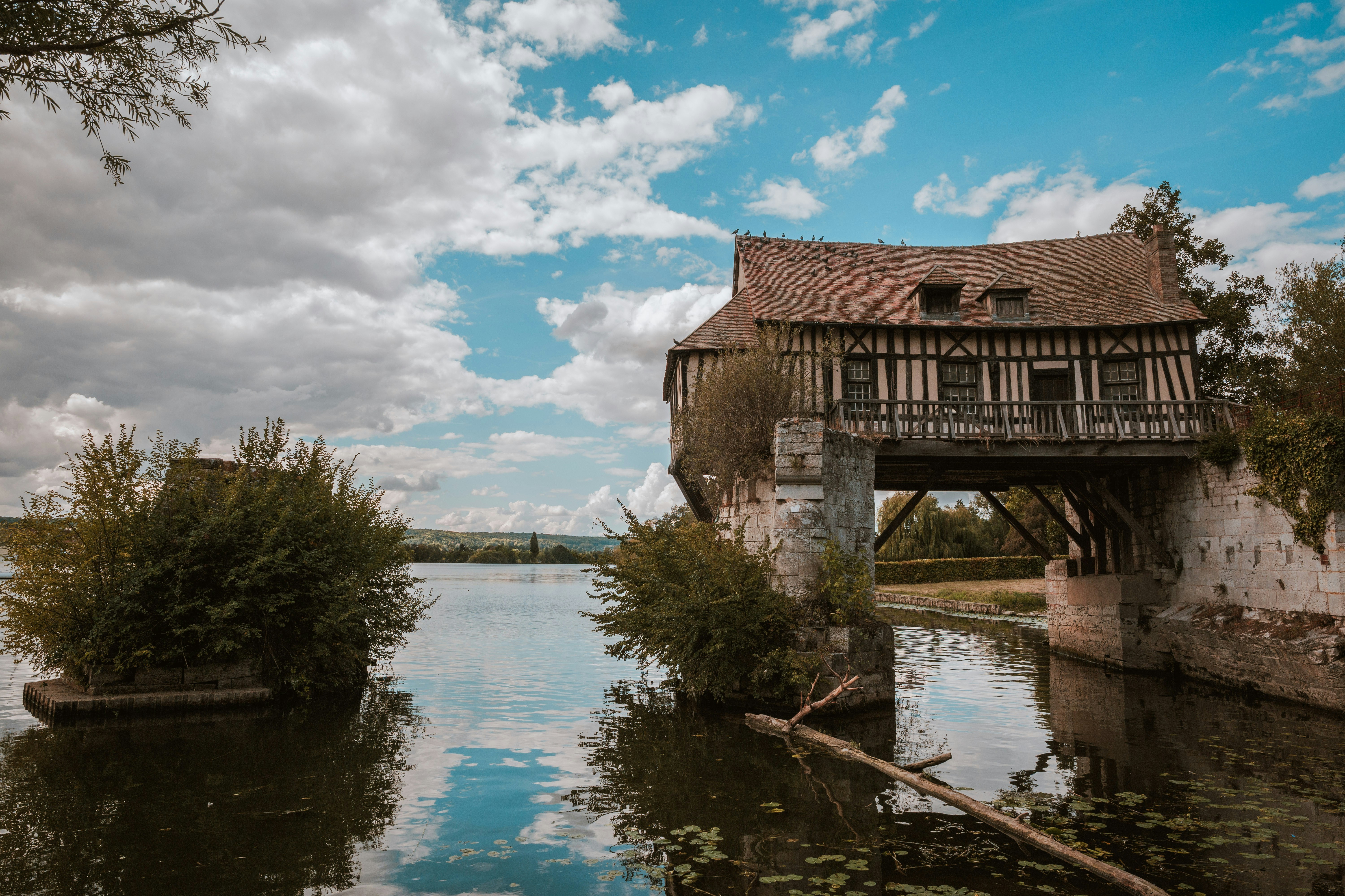 A half-timbered house built over a river with stone supports and a cloudy sky