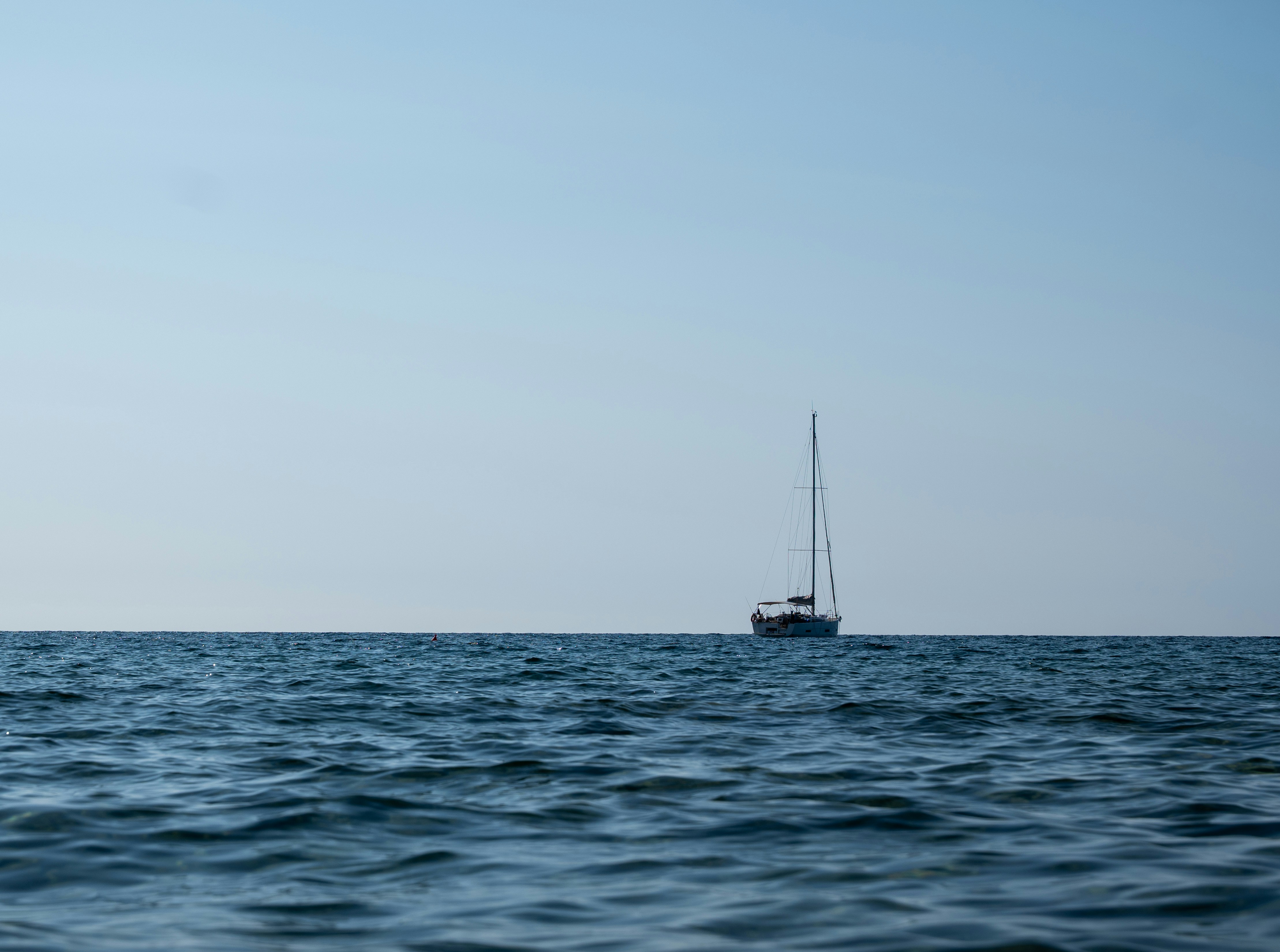 A sailboat on the horizon of a calm blue sea under a clear sky