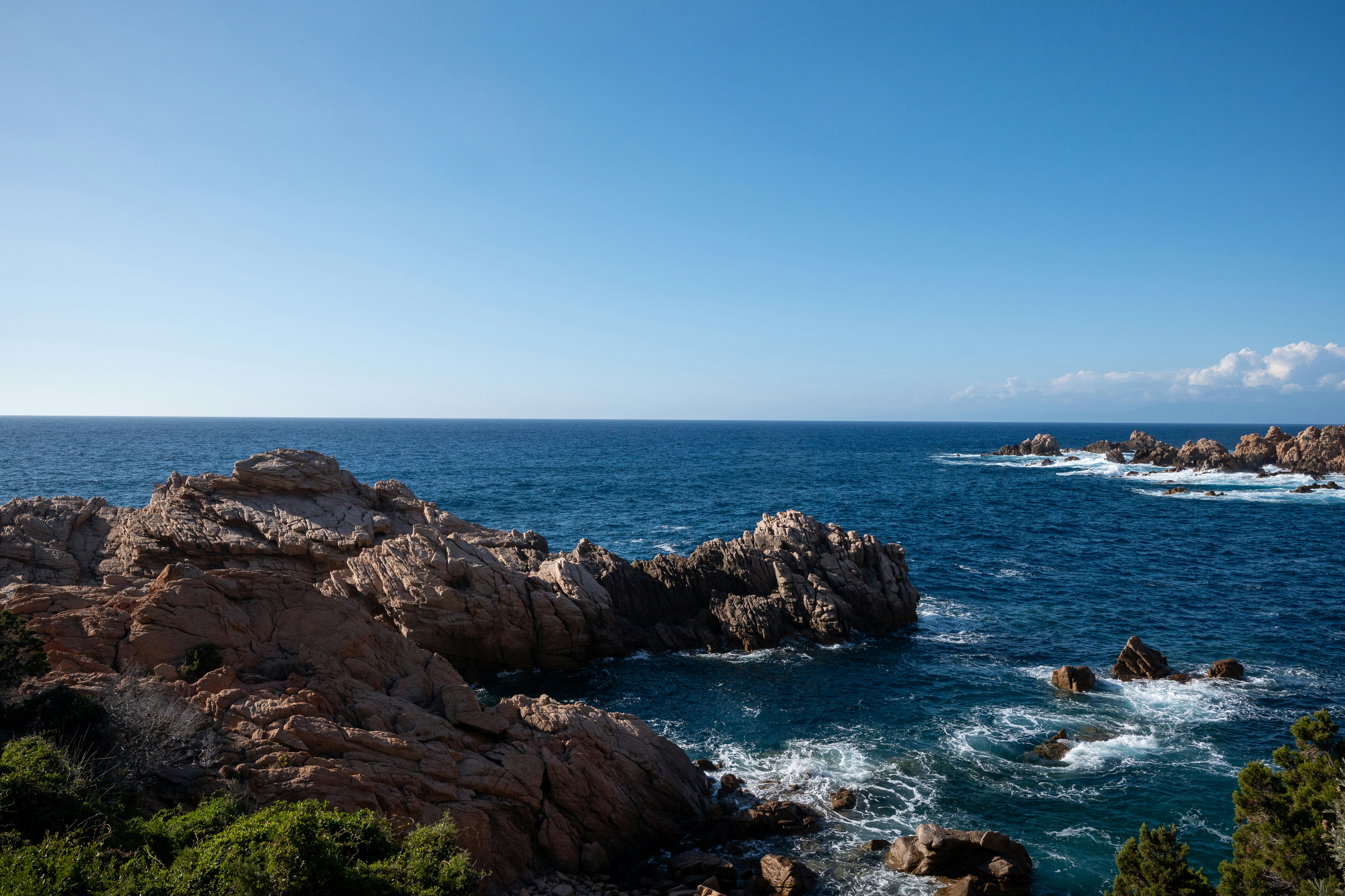Jagged orange rocks along a deep blue sea under a clear sky