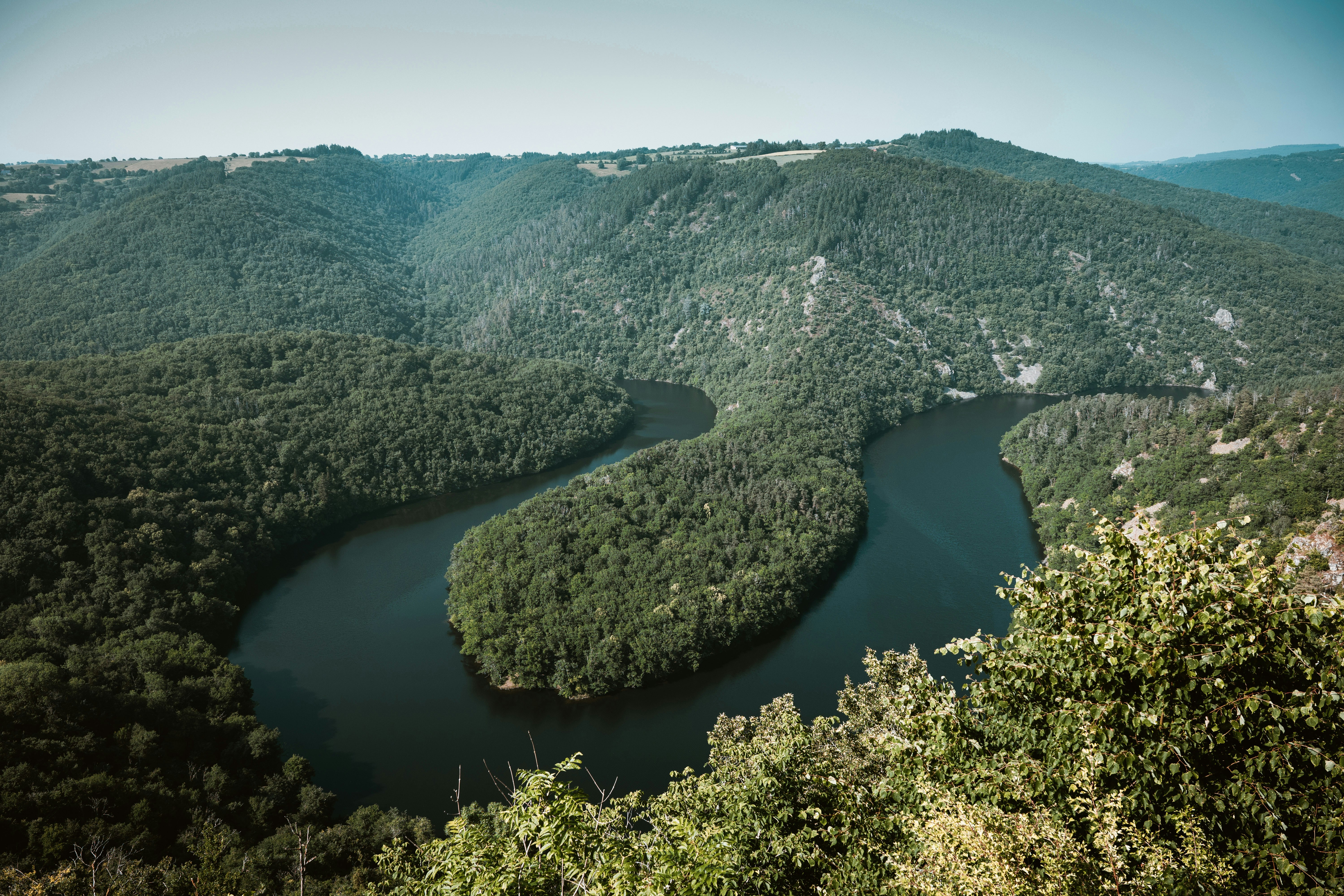 A winding river flowing through a deep valley covered in dense green forest