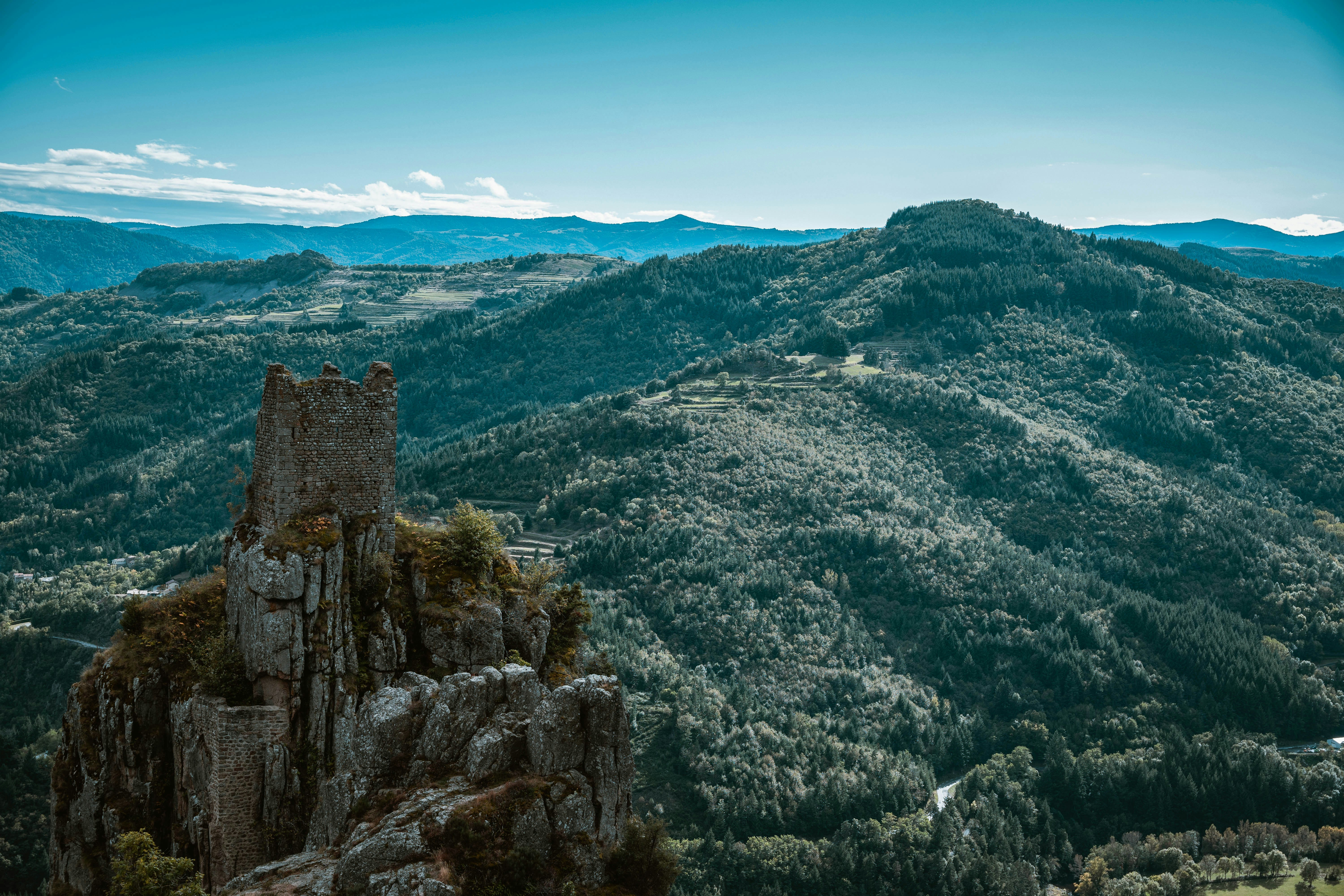 A stone castle ruin on a rocky cliff overlooking a vast forested valley