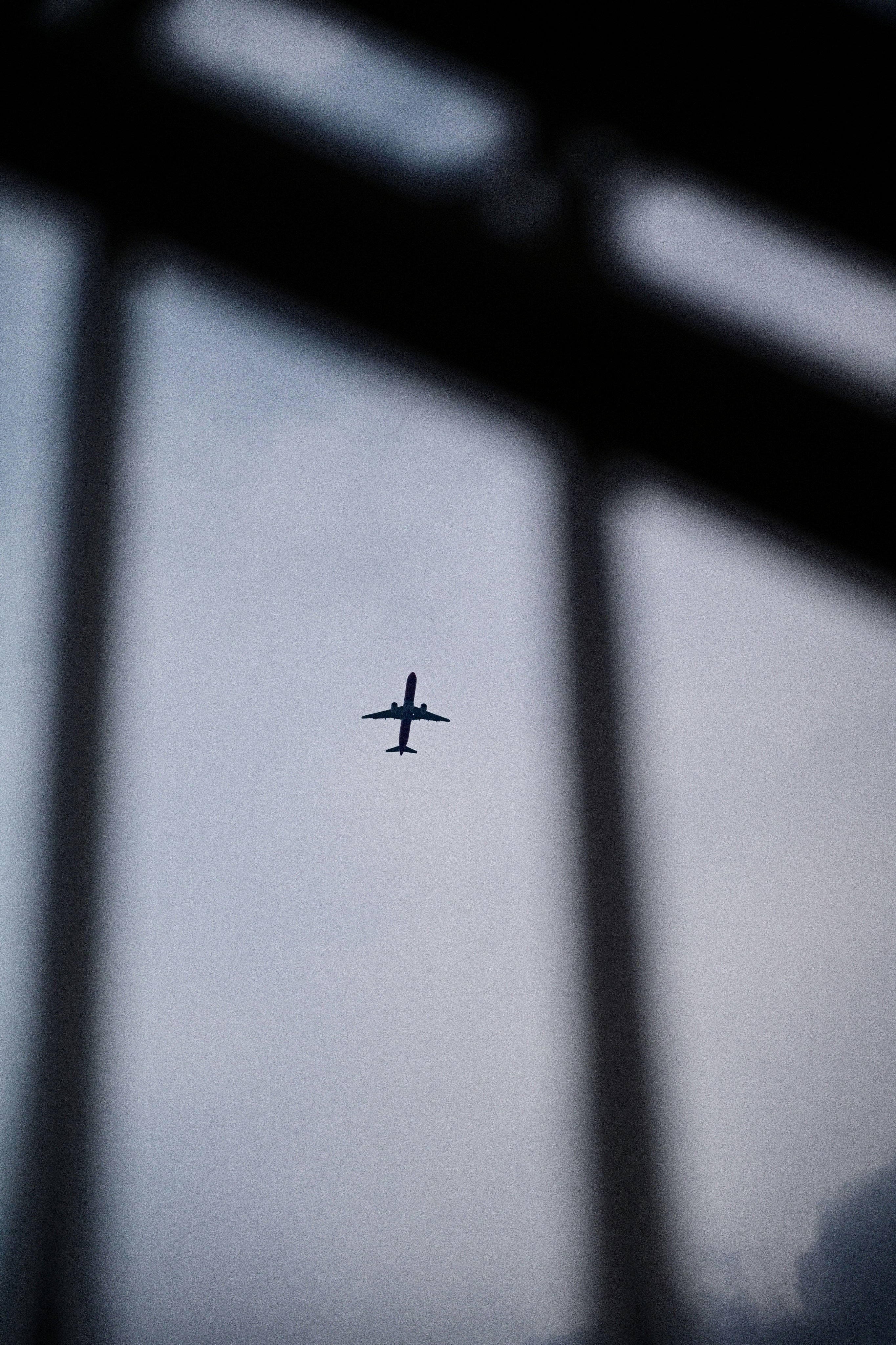 A silhouette of an airplane flying across a grey sky behind window frames