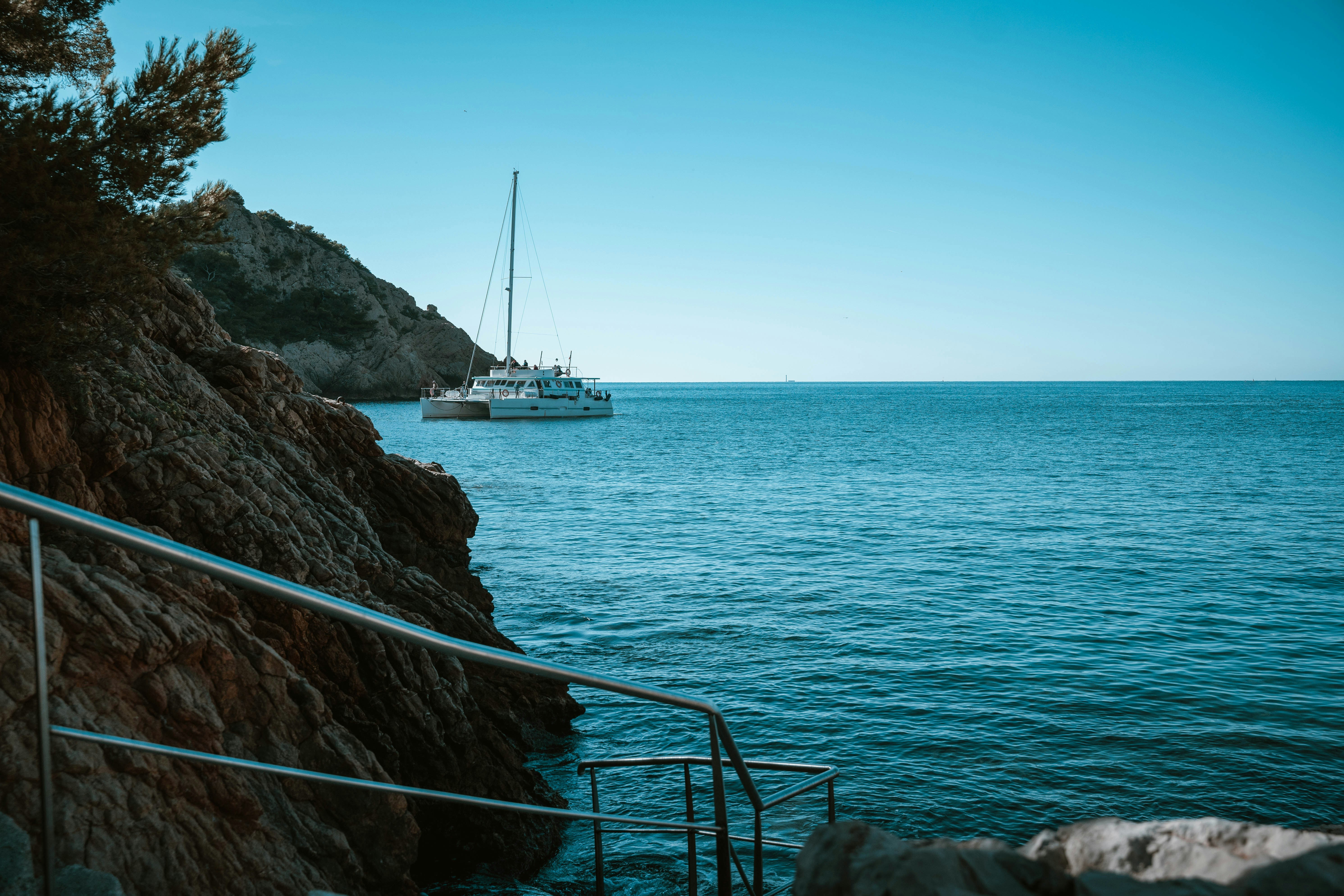 A white catamaran sailing on blue water near a rocky cliffside