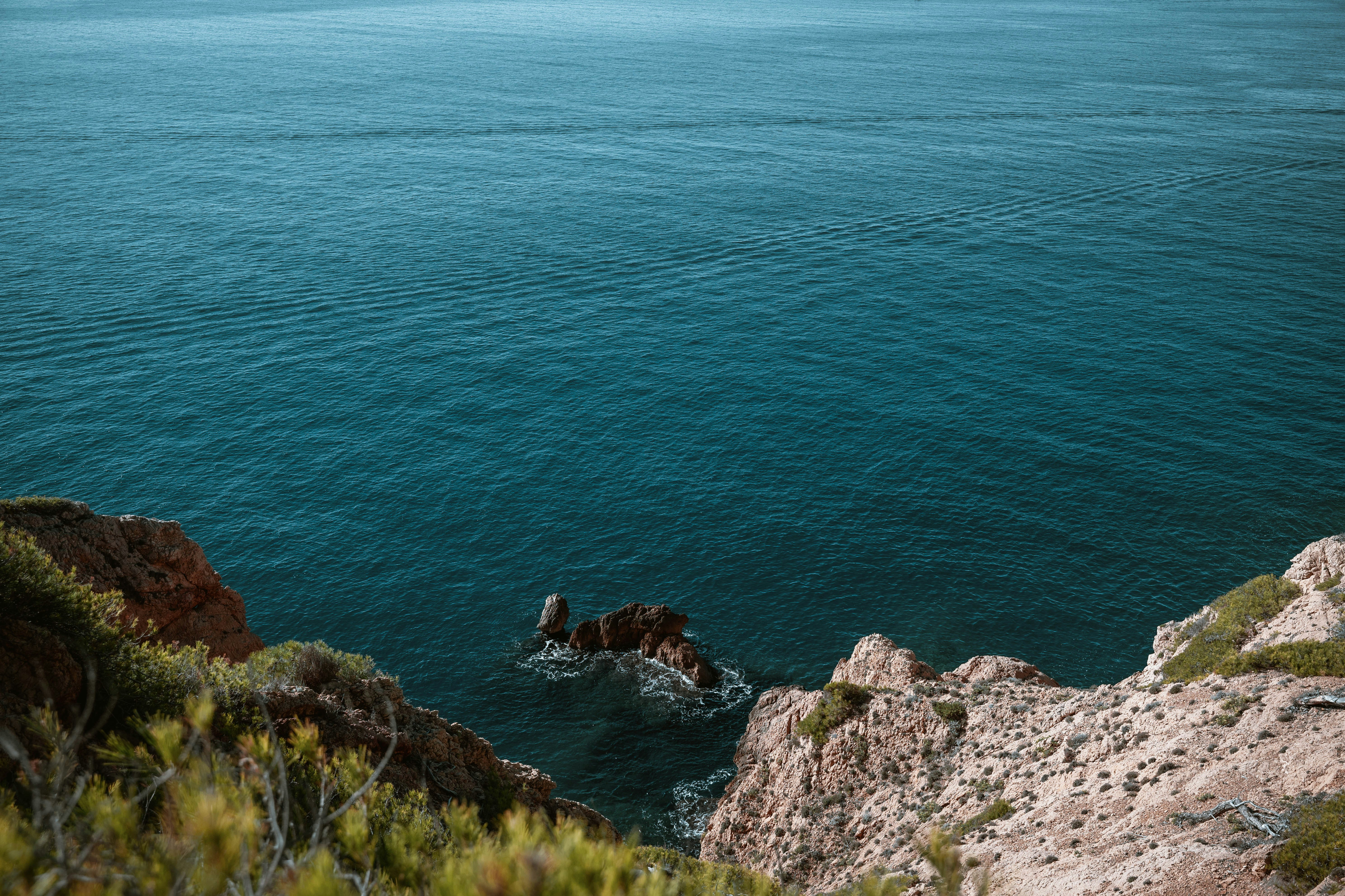 A rocky cliff overlooking deep blue ocean water with a small island