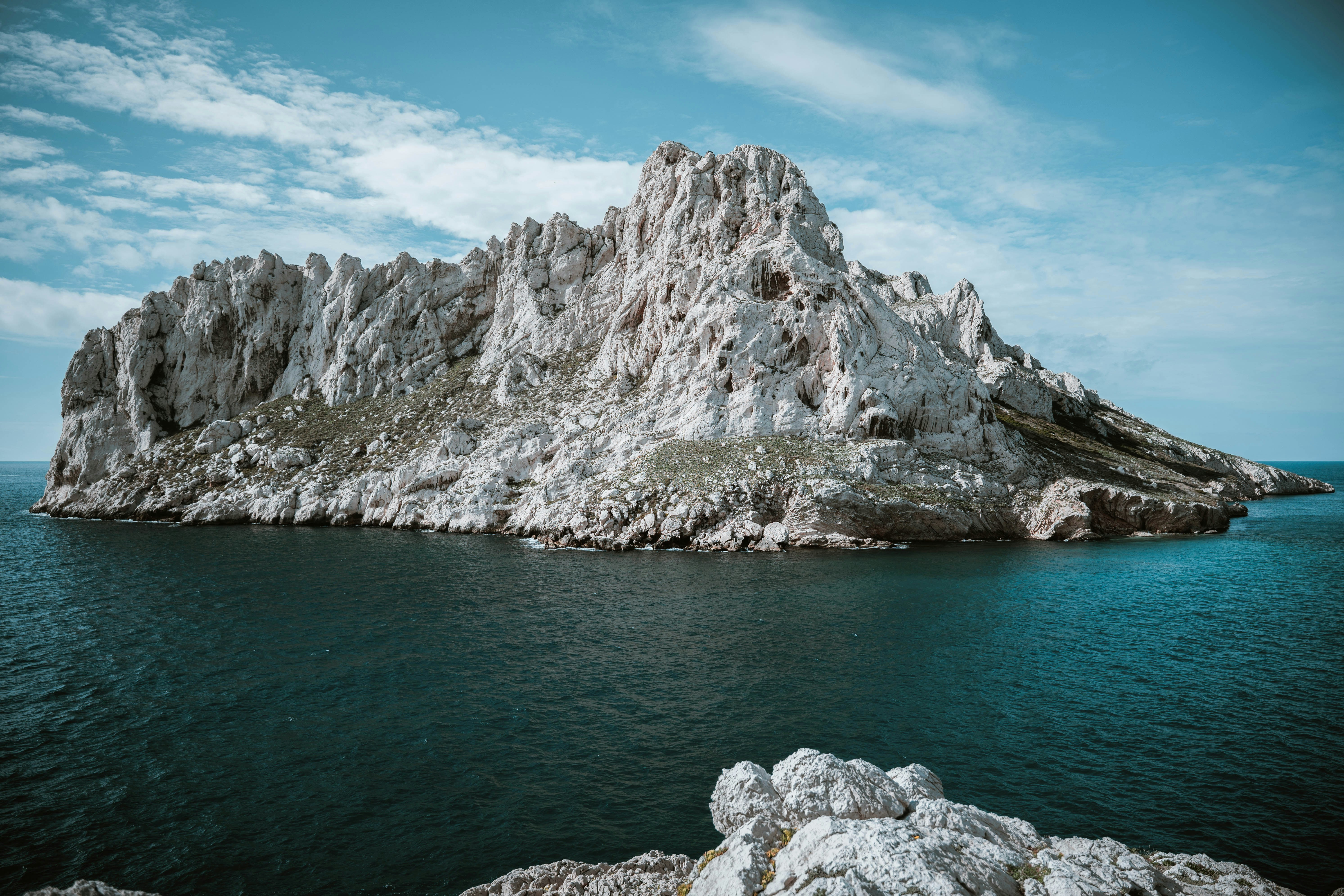 A jagged white limestone island rising from deep blue sea under a cloudy sky