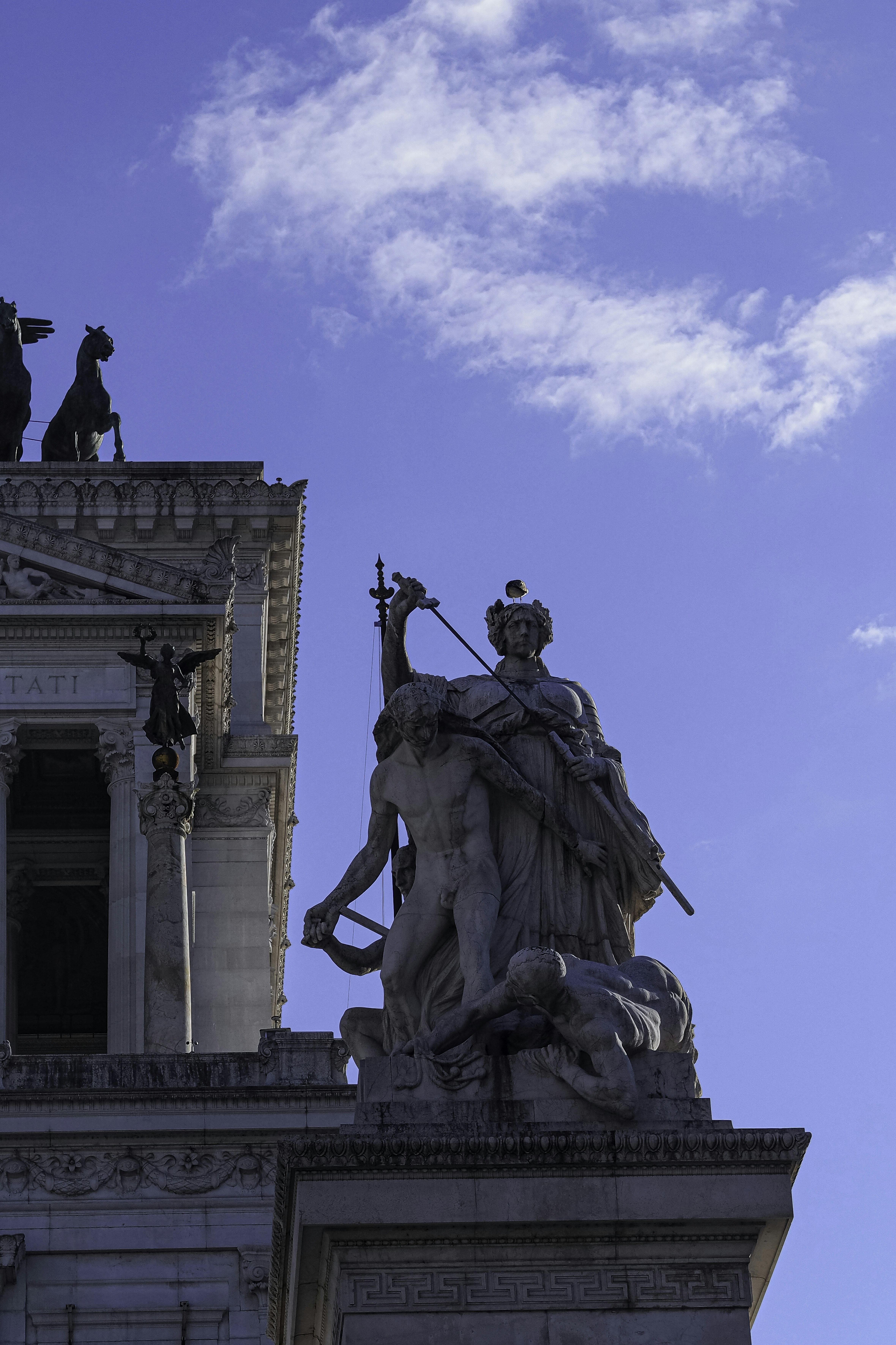 Stone statues of figures with a sword against a blue sky in Rome